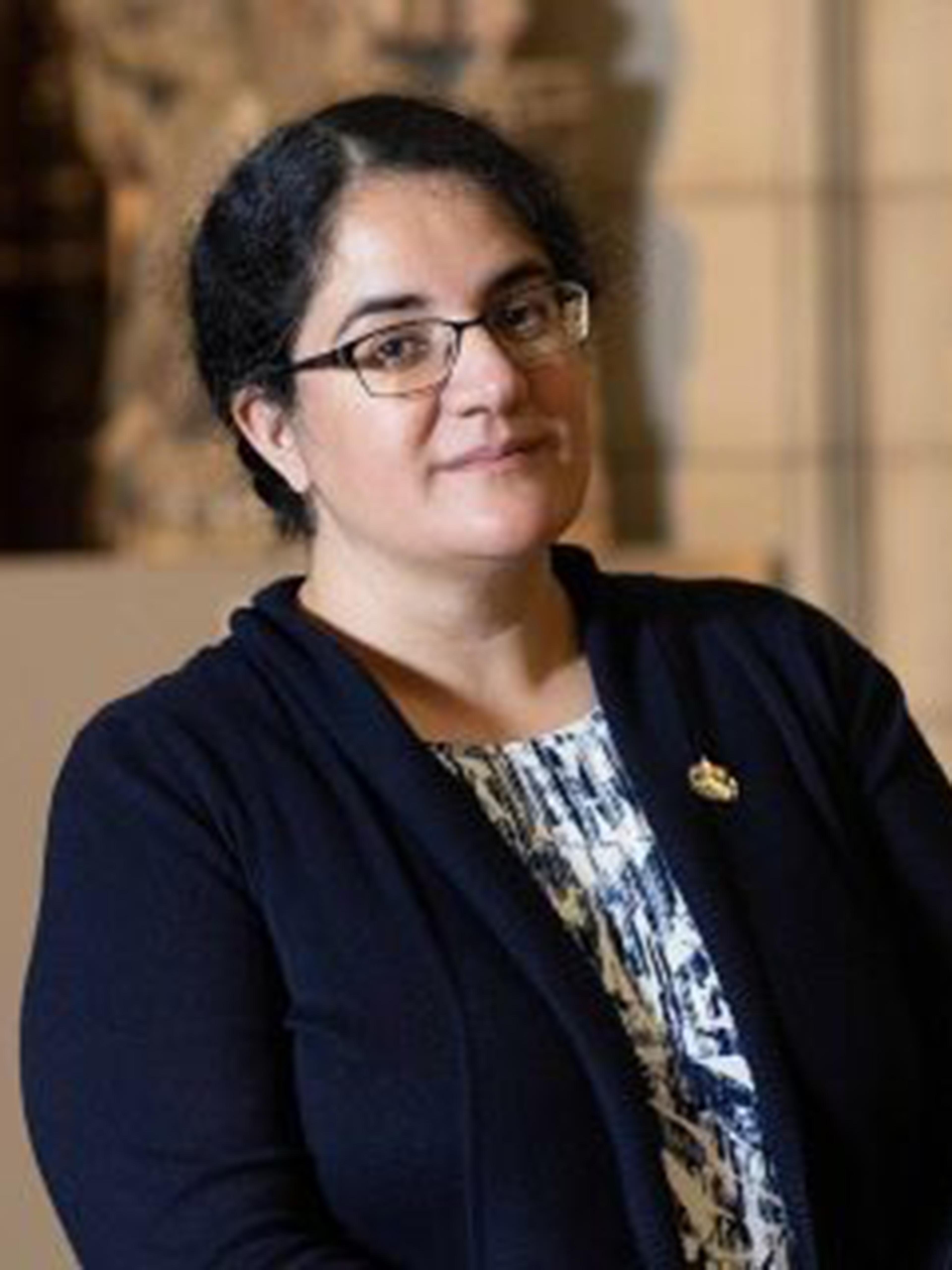 A woman wearing glasses and a dark sweater poses in an art gallery