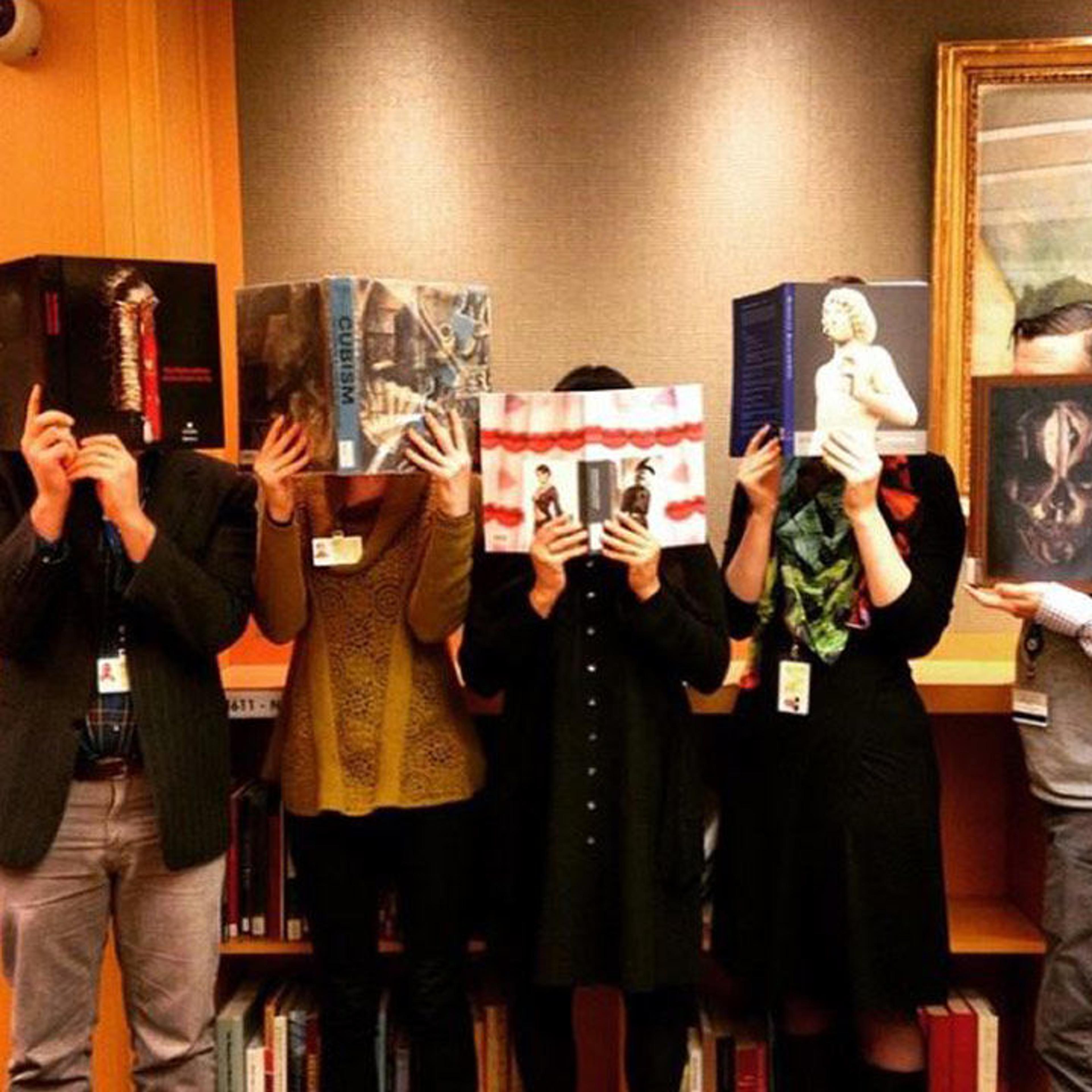 Five librarians with books in front of their faces