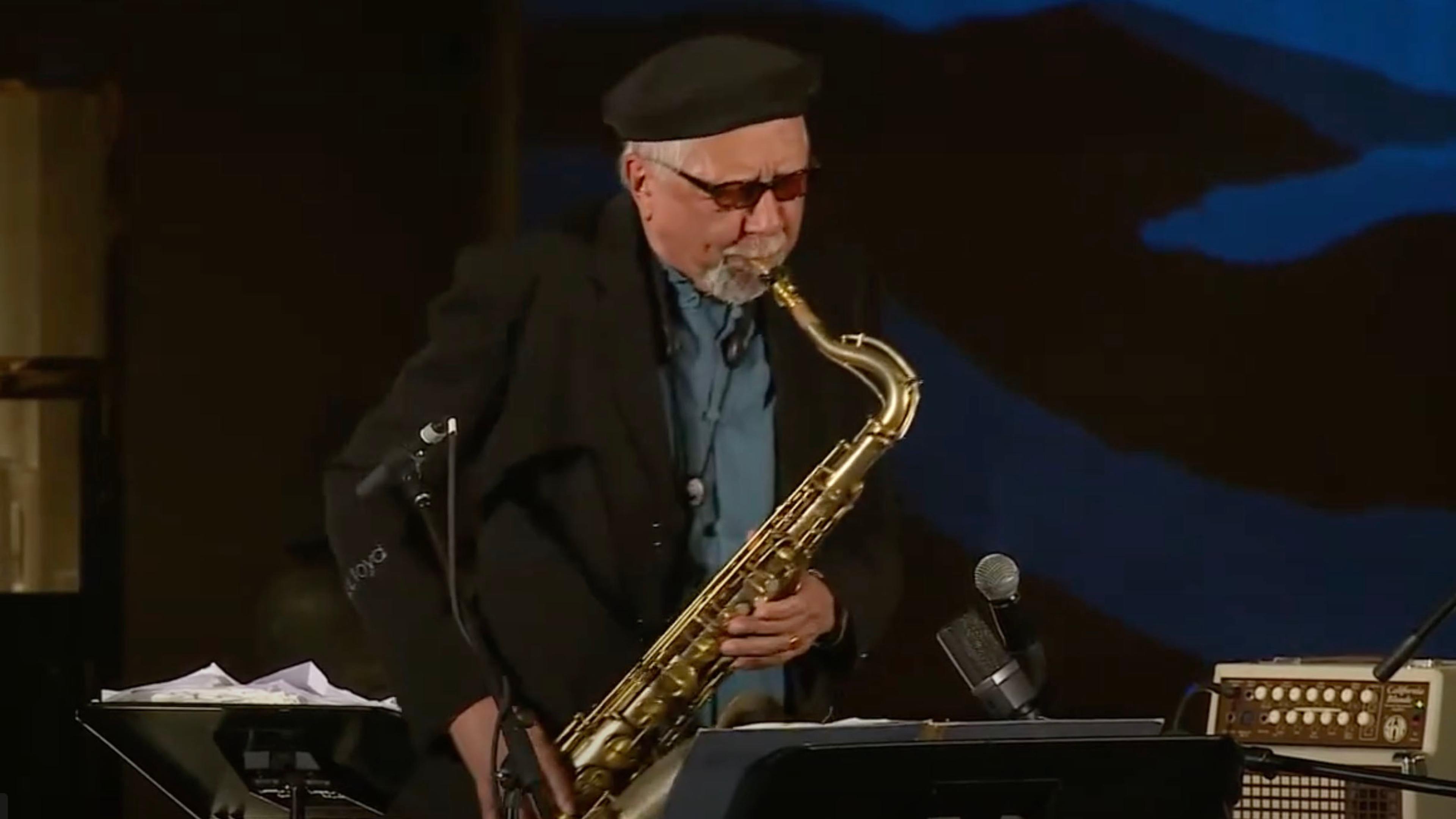 Man wearing a black beret playing the saxophone onstage