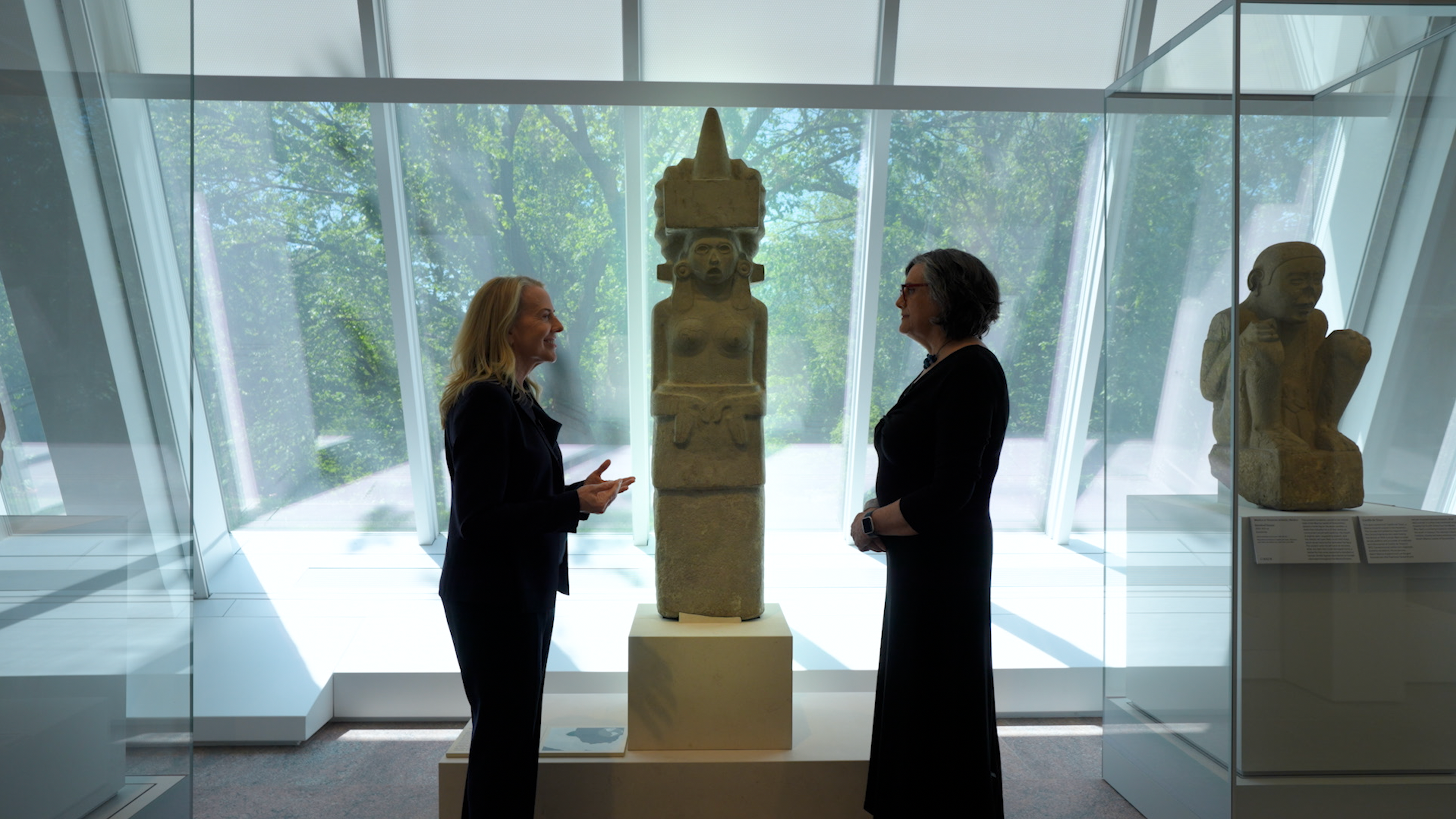 Joanne Pillsbury and Laura Filloy Nadal standing in front of a female sculpture in the Ancient Americas galleries of the Michael C. Rockefeller Wing