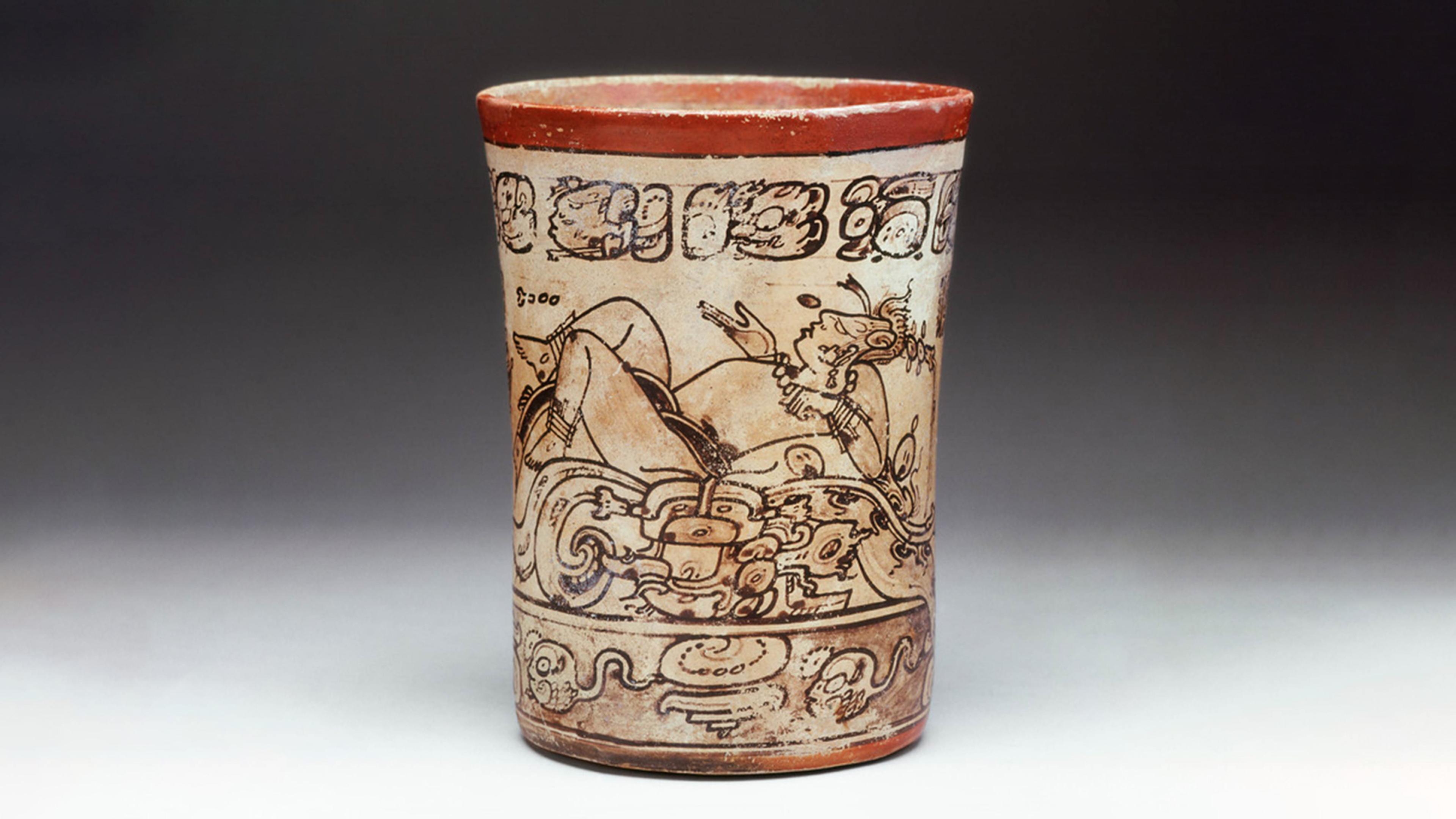 Image of cylindrical vessel with orange rim and tan body, with illustration of the Maize God on surface surrounded by patterns.