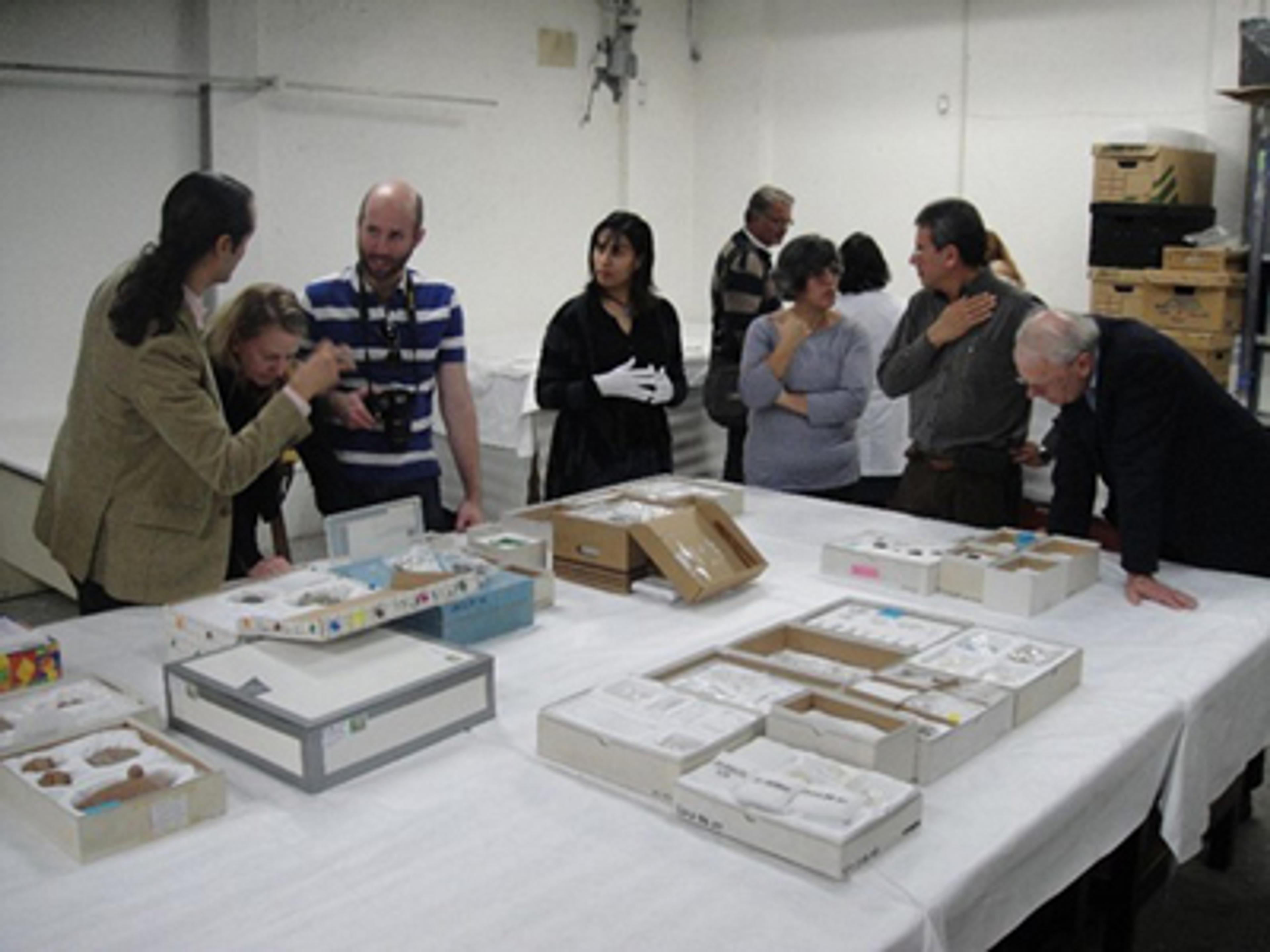 A group of art scholars, archaeologists, and researchers convene around a table to view artifacts under discussion