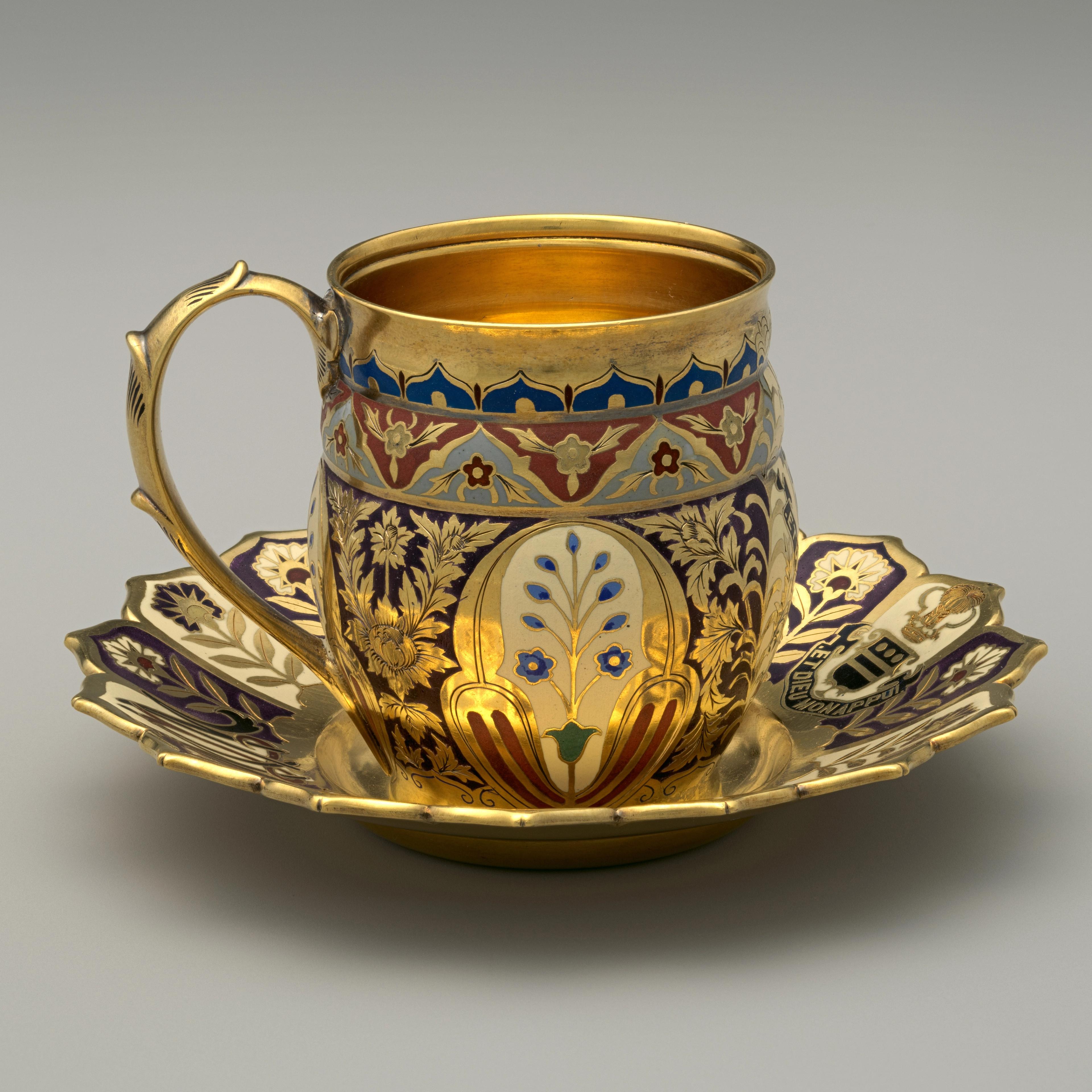 A pair of dazzling gilded and enameled cups and saucers adorned with floral designs, a coat of arms, and monogram.
