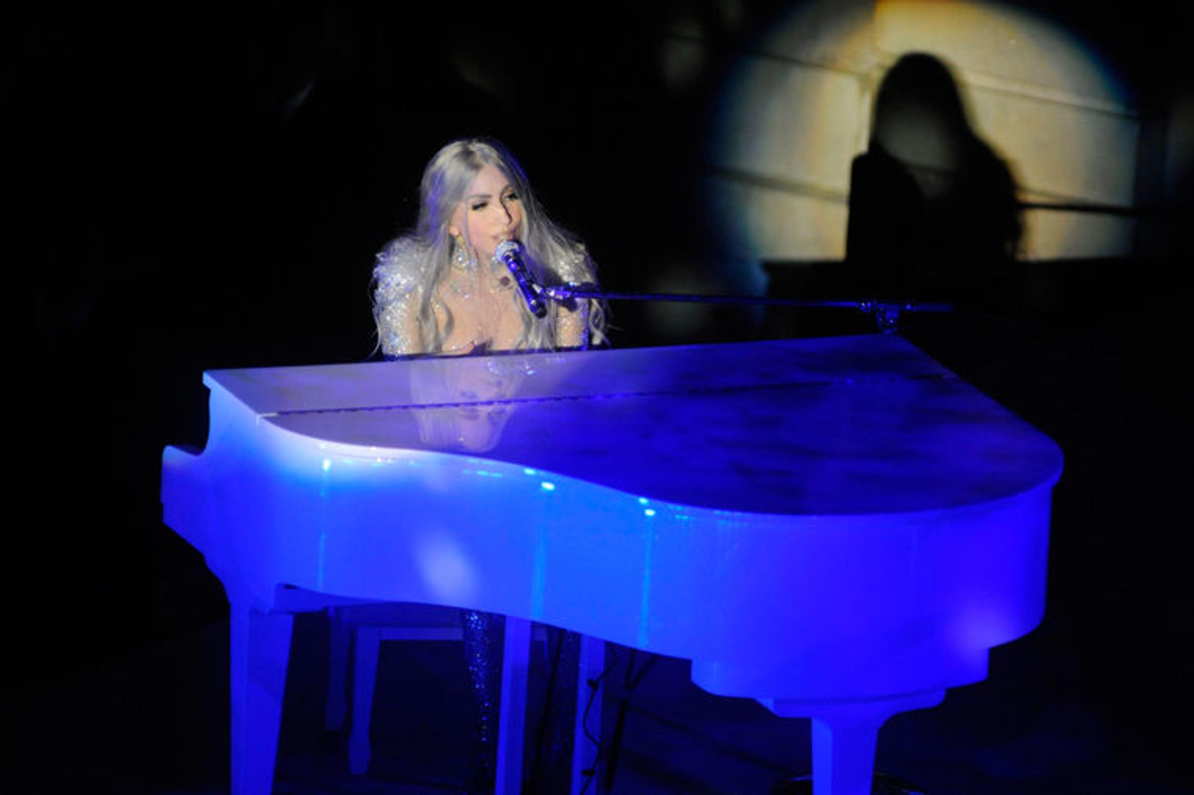 Lady Gaga performs while seated at a blue-lit piano