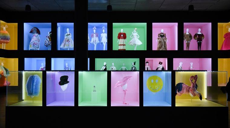 installation view of multiple fashion accessories from the exhibition with full ensembles in the background.