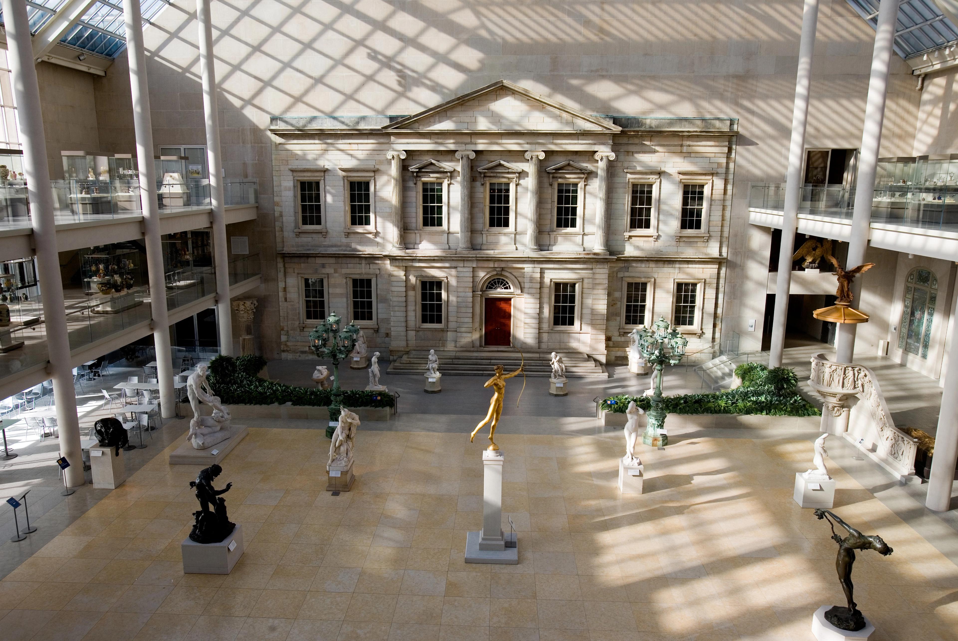 View of the Engelhard Court with sunlight streaming in from the upper windows. Statutes dot the floor space, while a classical building facade dominates the background.