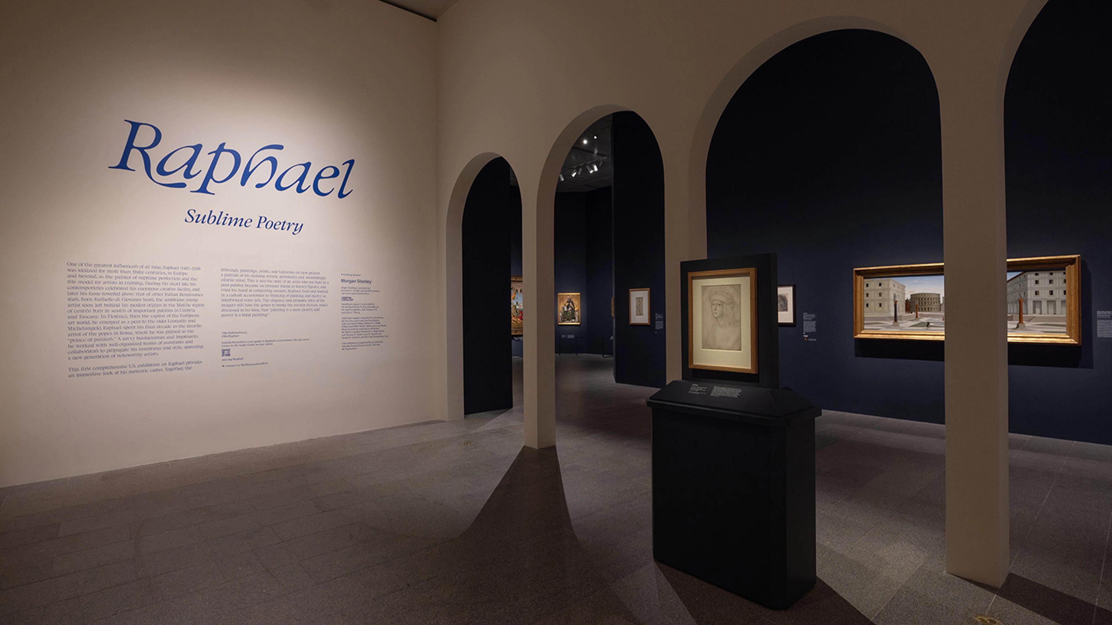 Exhibition room with a wall reading "Raphael: Sublime Poetry." Dim lighting highlights framed artworks