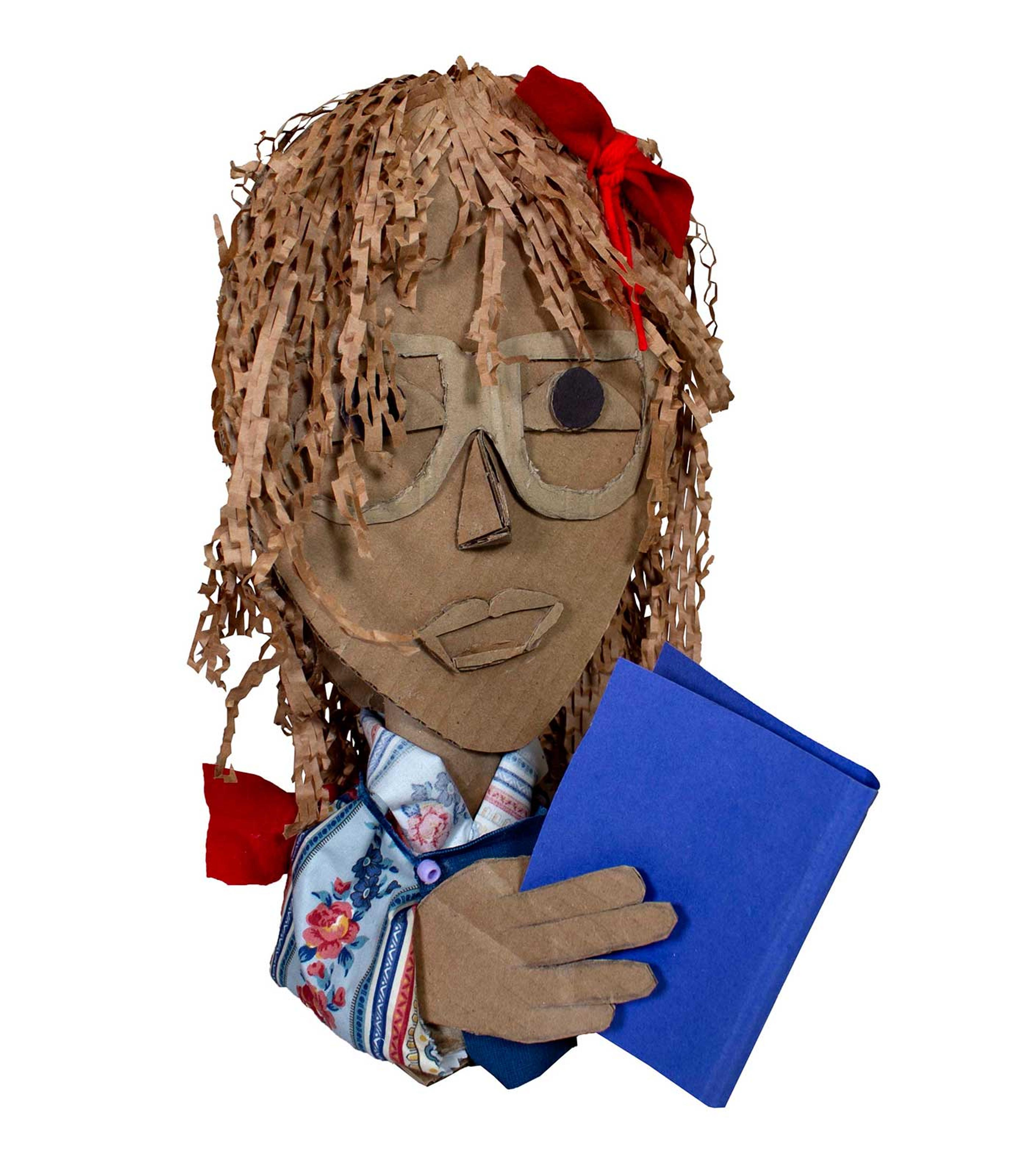 Cardboard, paper, and cloth scultpure of a child wearing glasses reading a blue book.