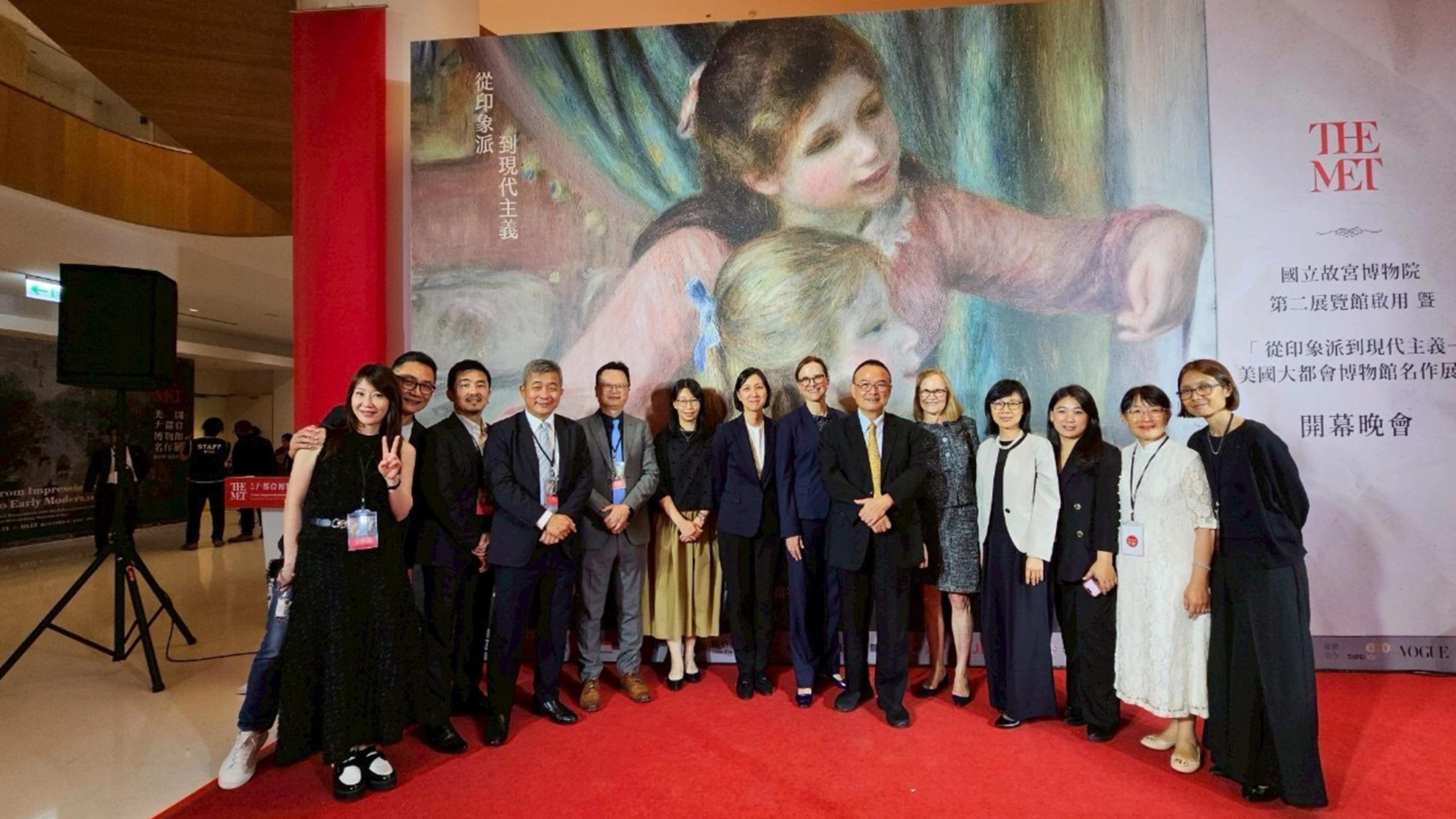 A group of individuals standing front of a large poster for Met objects on exhibit in Taiwan.