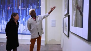 Mamadou Diouf standing by Alisa LaGamma and gesturing to the photo wall in the Arts of Africa galleries