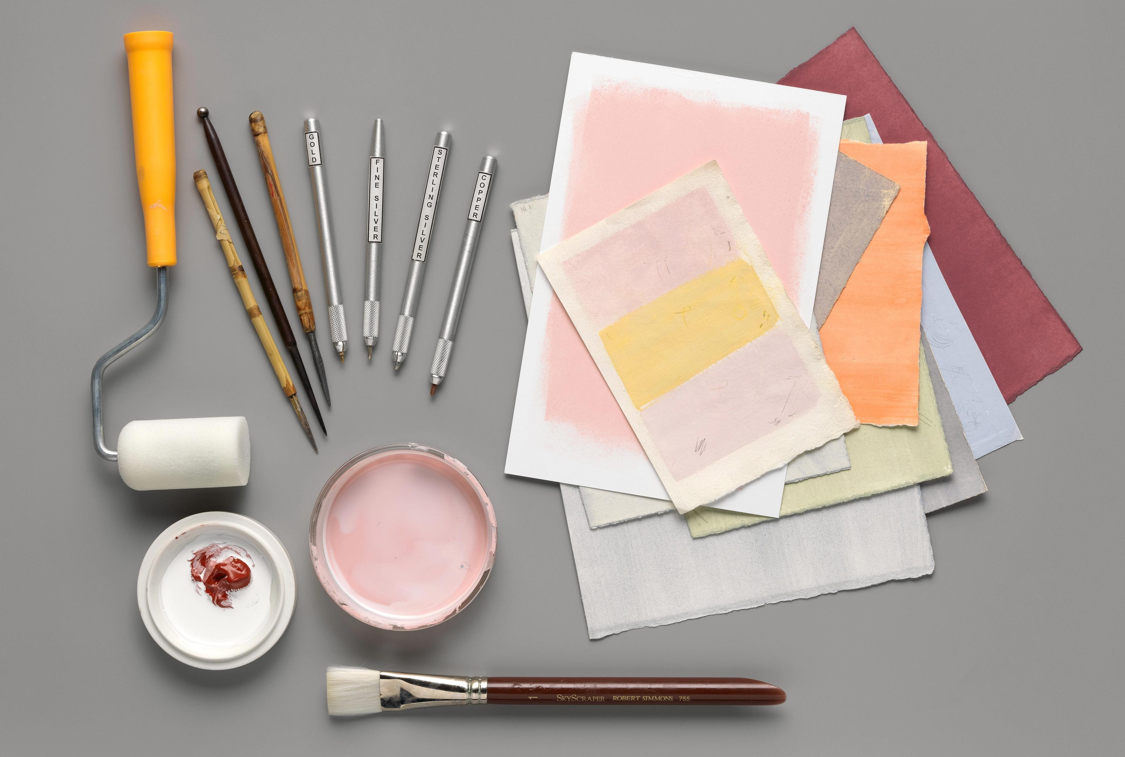 An artful arrangement of specialized tools for making metalpoint drawings beside a stack of colorful paper.