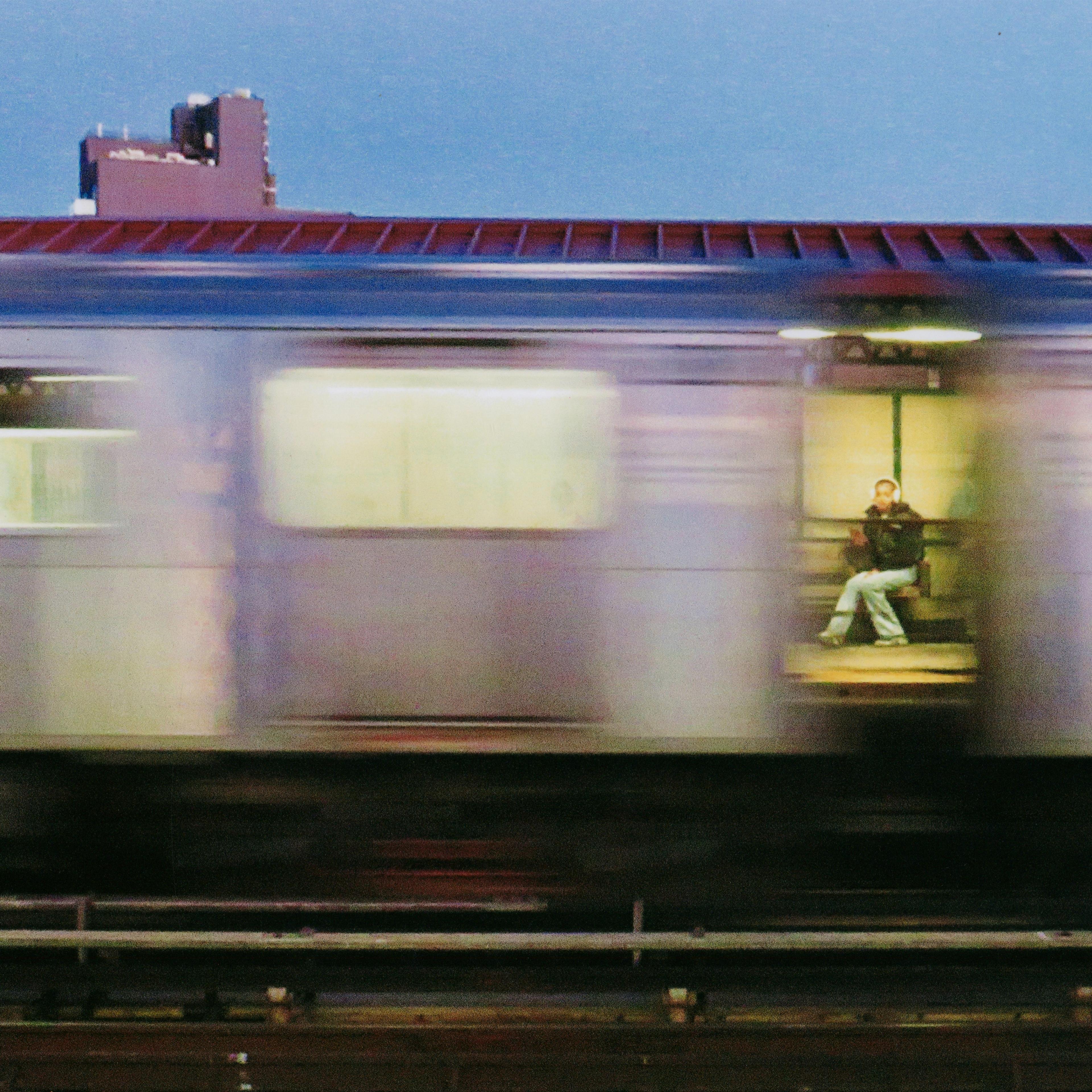 Moving photo image of a train, and in the between carts sits a woman.