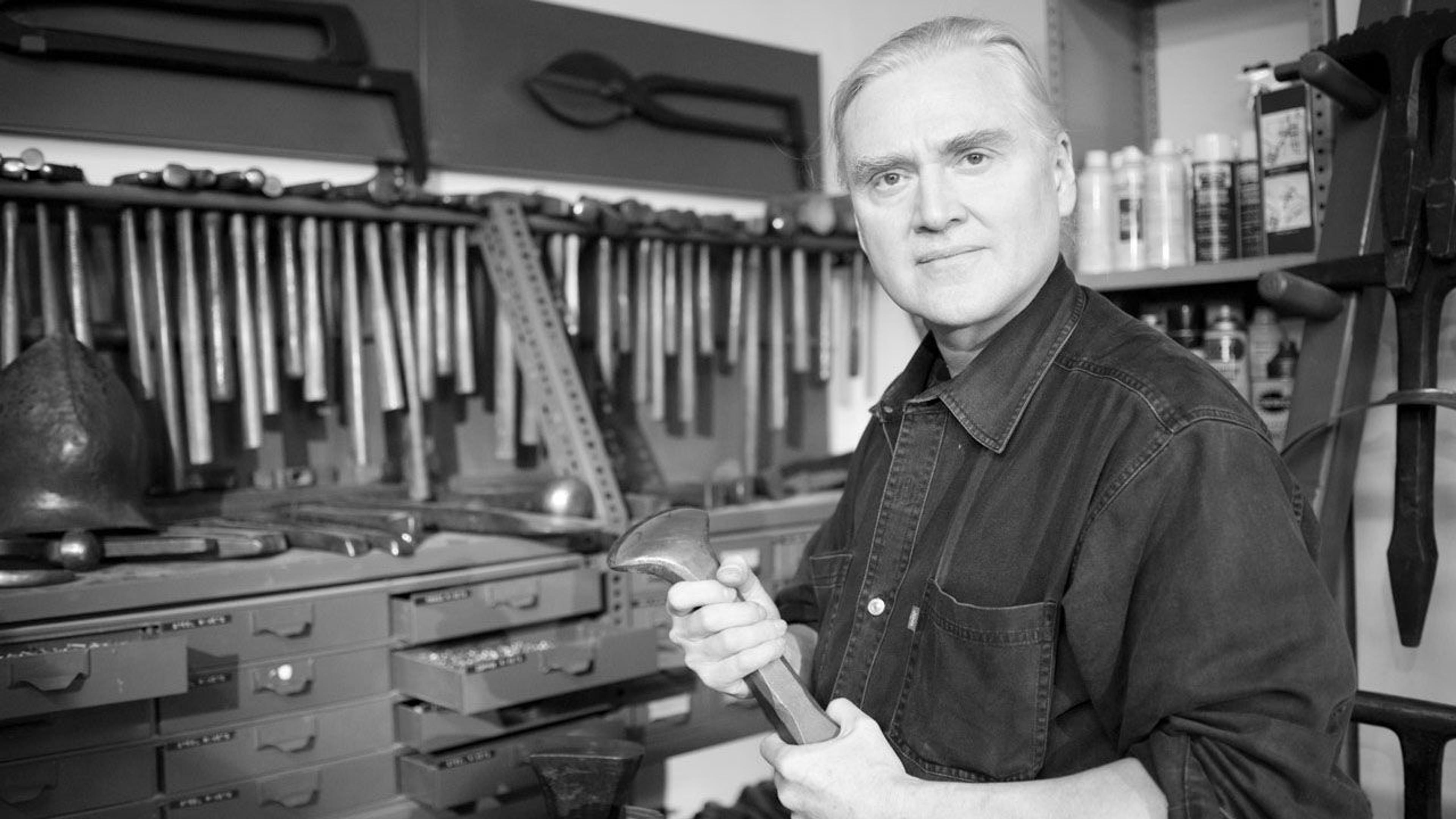 Black and white photograph of armorer Hermes Knauer standing in his workshop at The Met