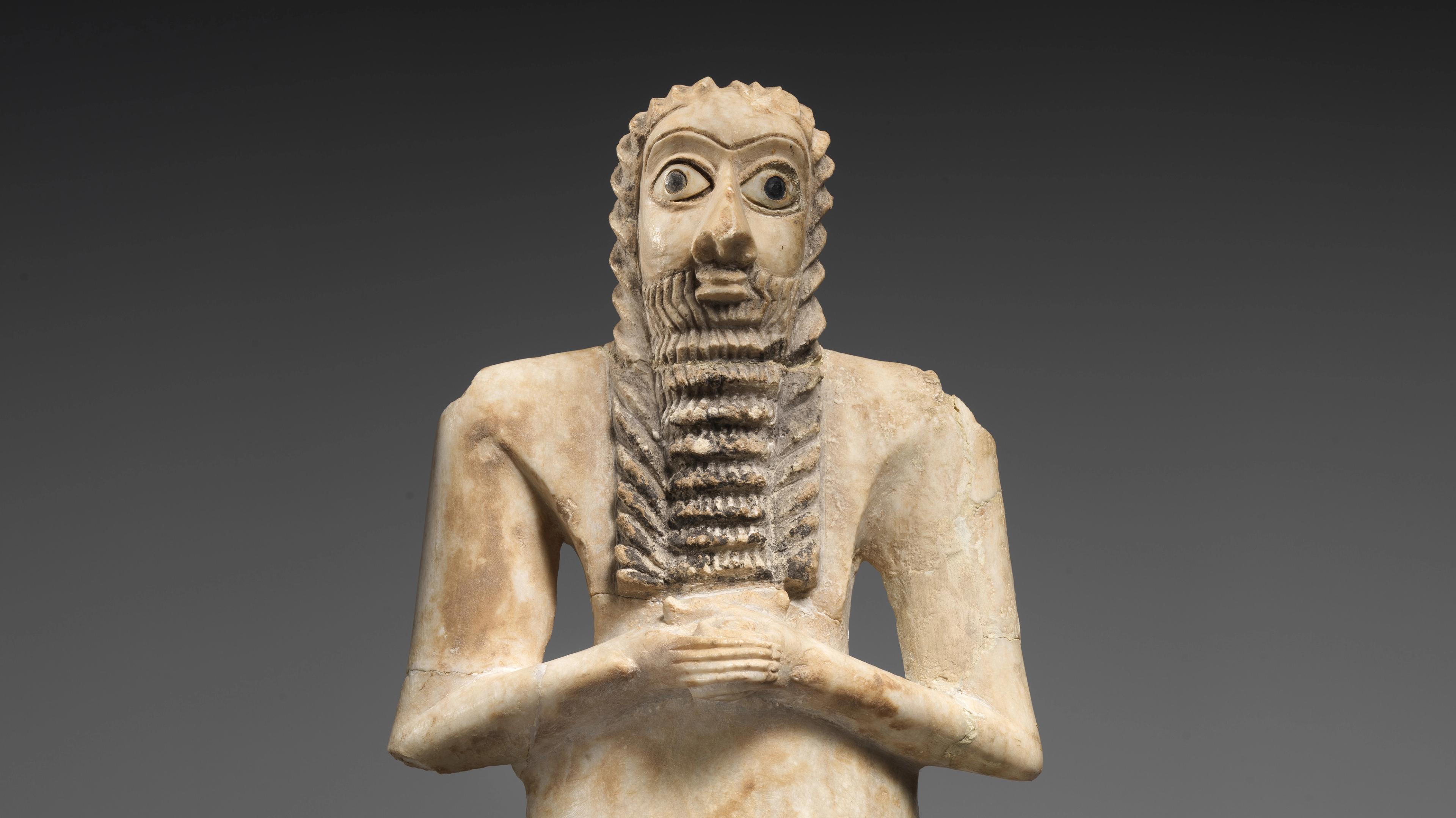 White stone figure with wide eyes and a long, ridged beard, clasping his hands across his chest.