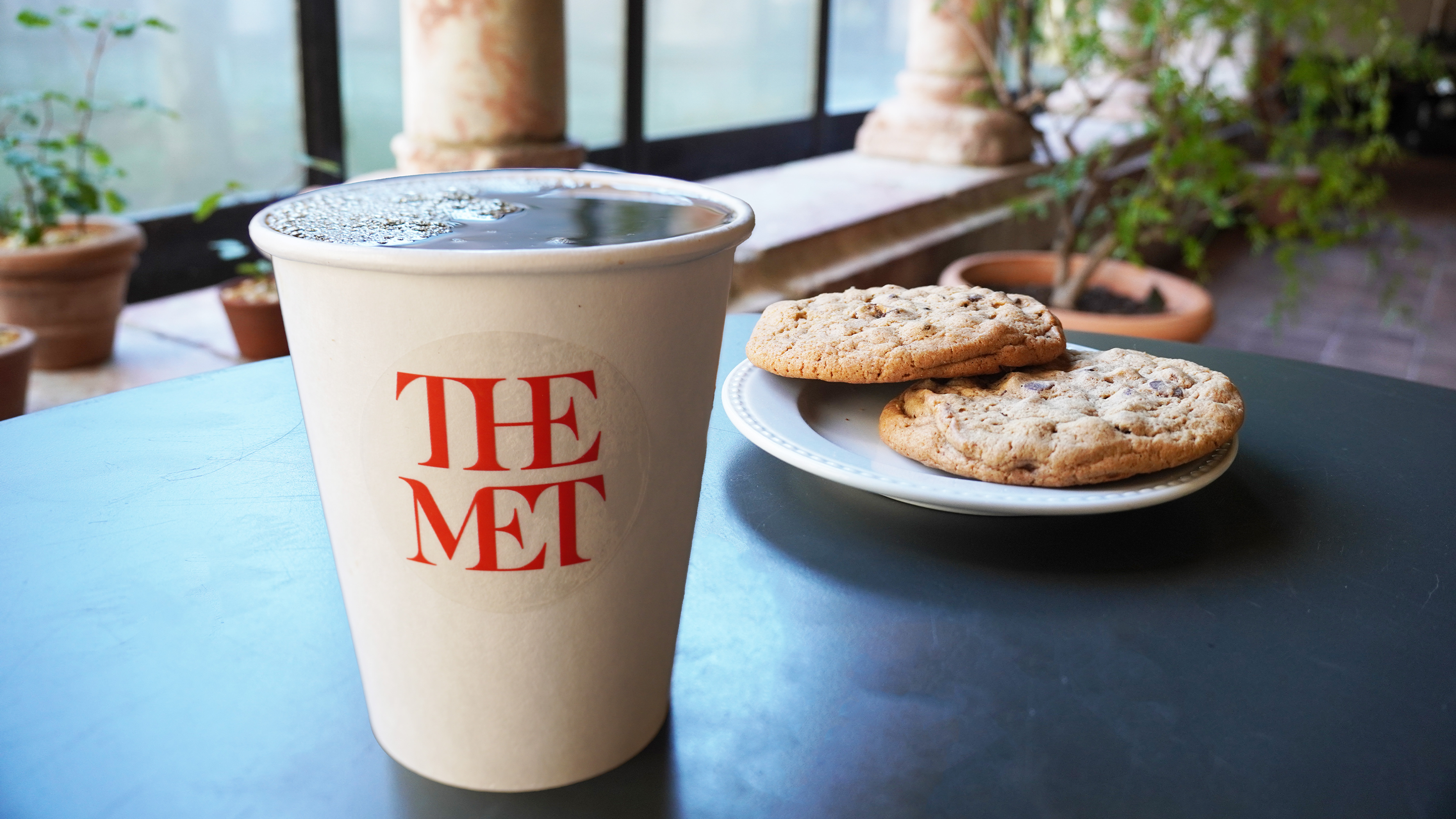  A coffee cup with The Met logo and a plate of cookies. 