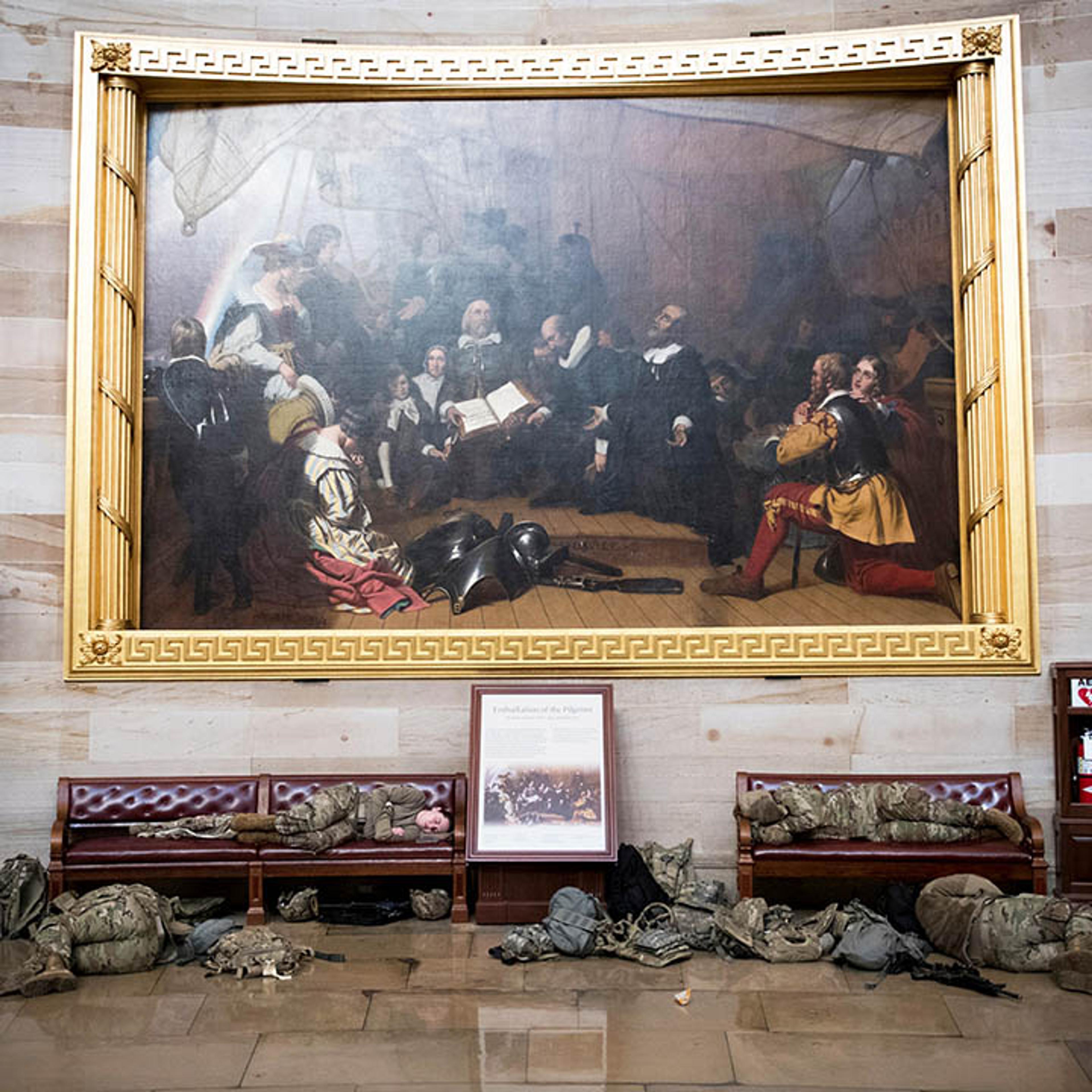 Soldiers sleeping in front of a large painting at the Capitol.