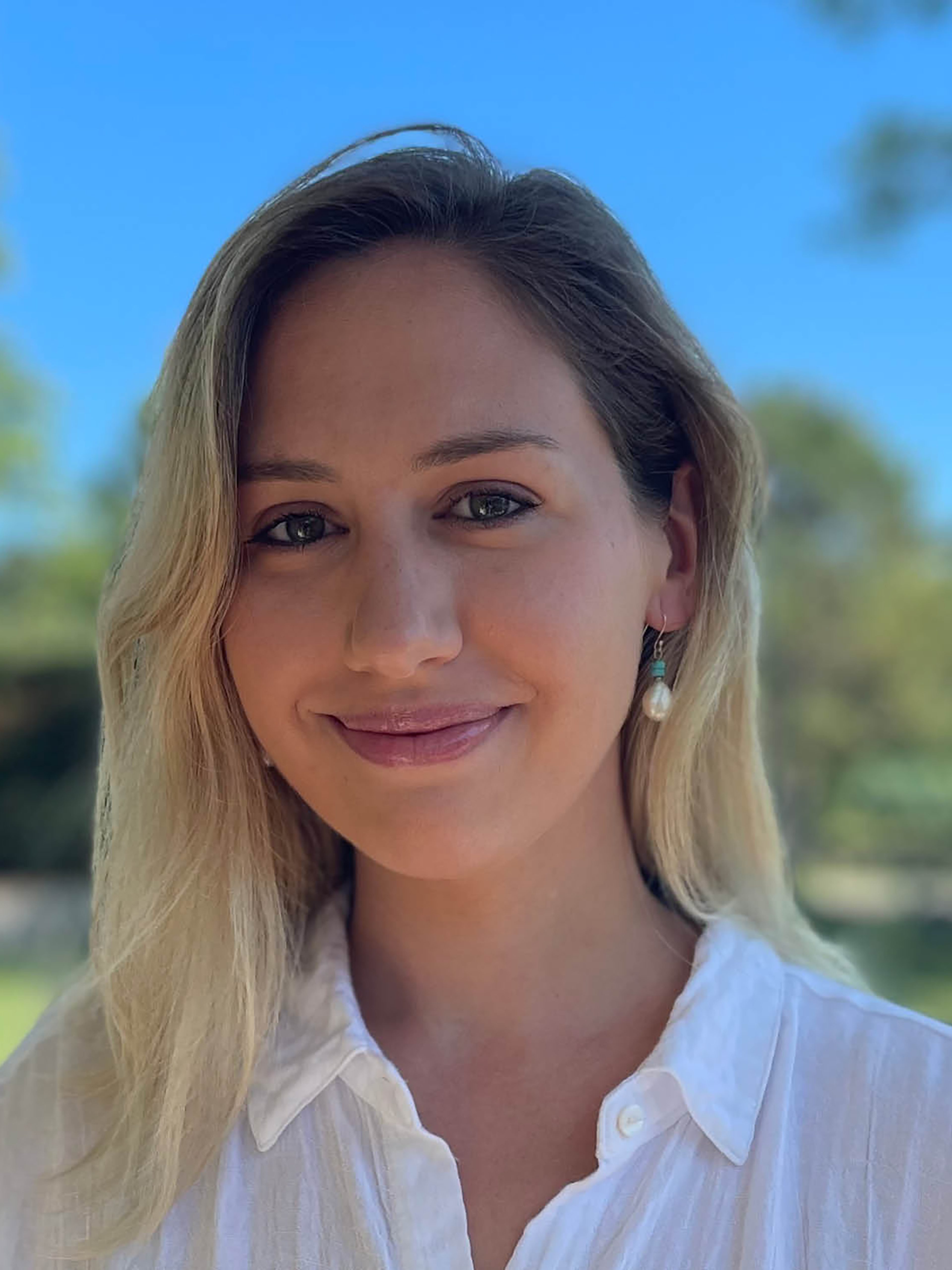A woman with blonde hair stands outside on a sunny day