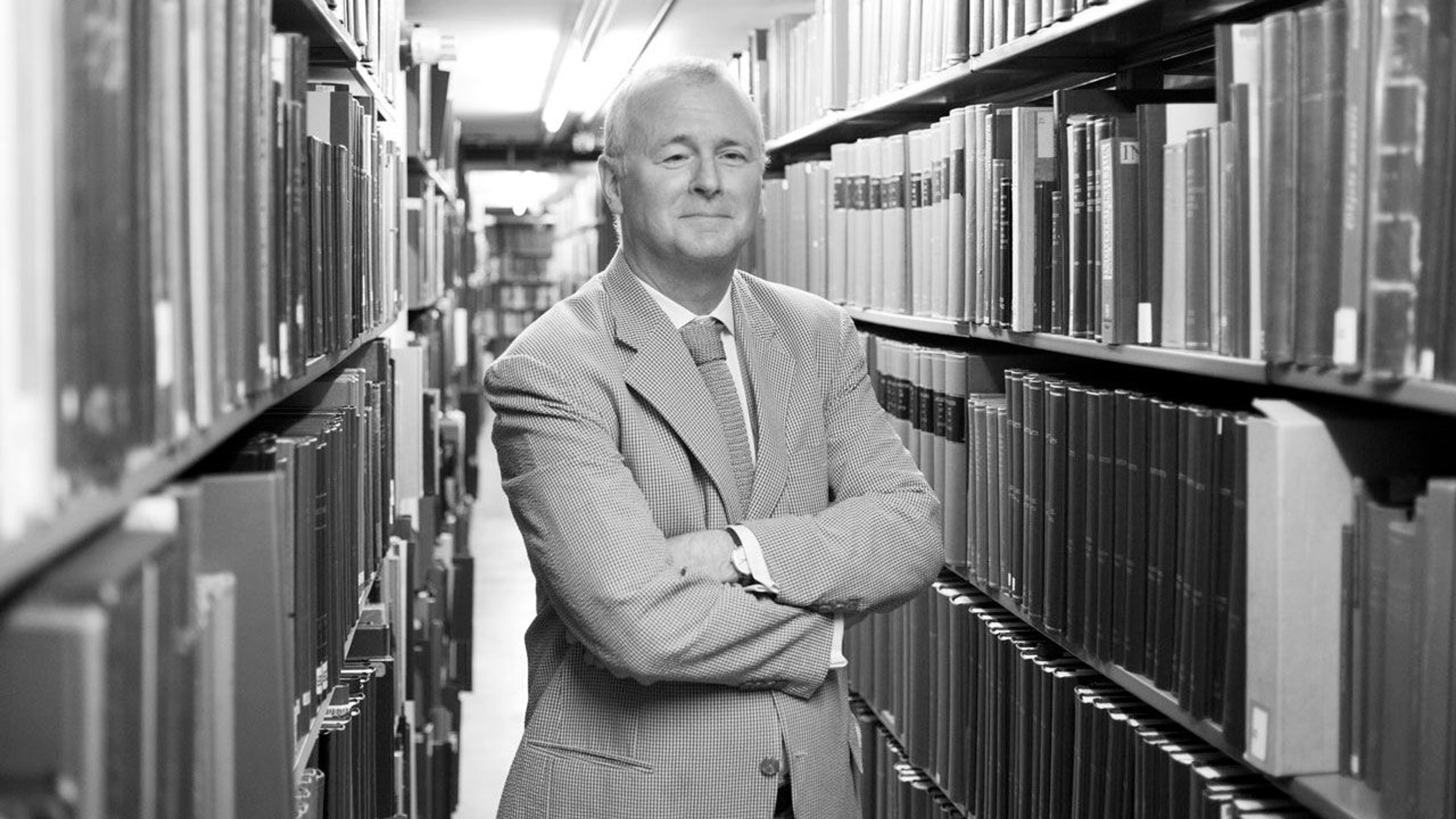 Black and white photograph of chief librarian Ken Soehner standing in an aisle in the library filled with books