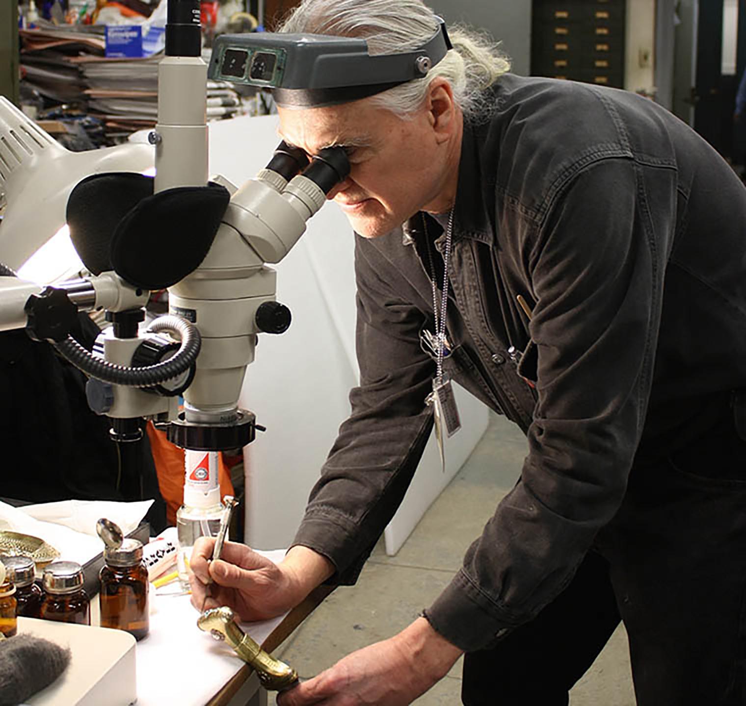 A conservator looking through a magnifying device to clean a dagger handle.