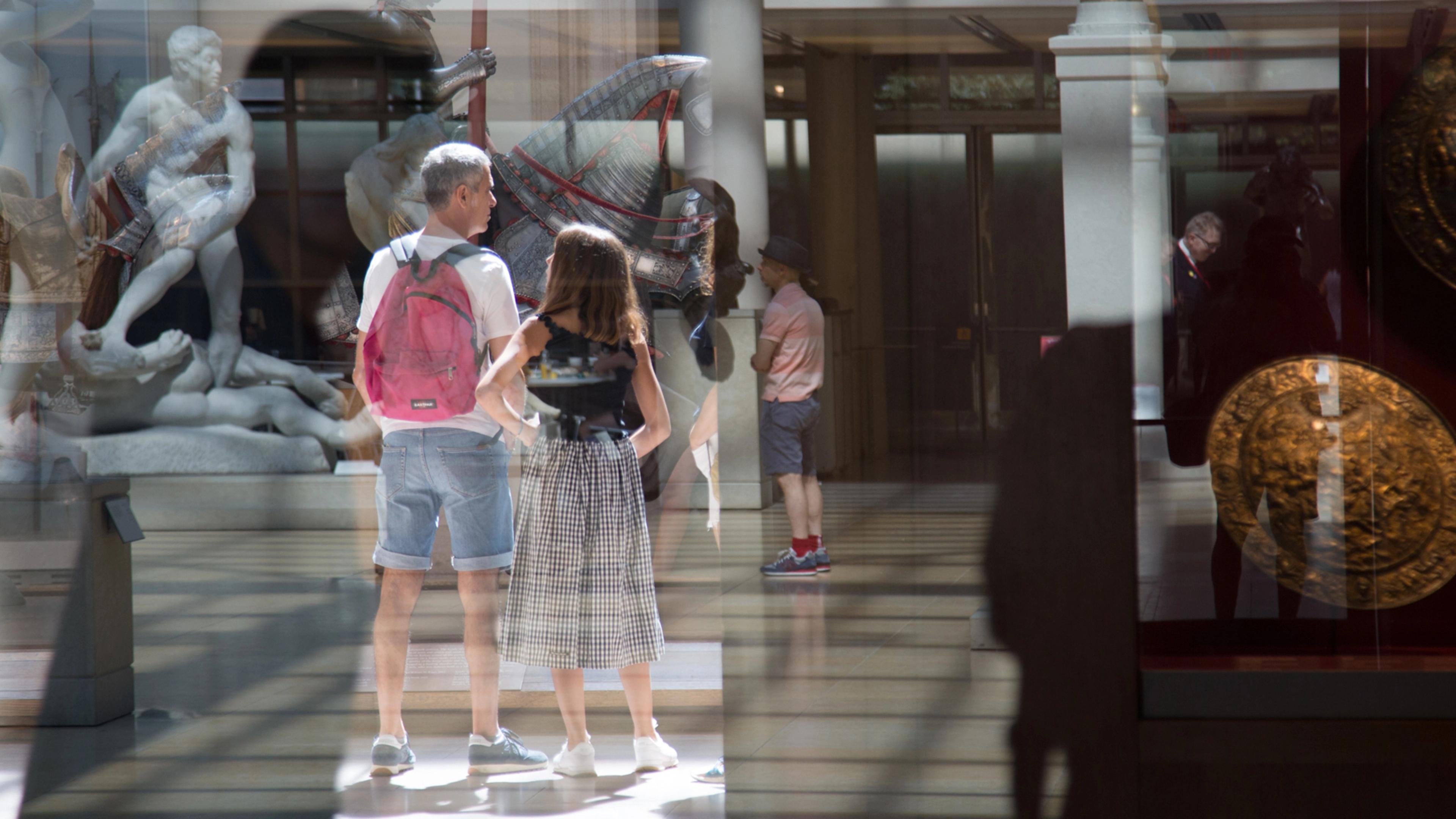 Photograph of reflecting stone sculptures, medieval armor, a round shield, and Museum patrons  in the sunlit Engelhard Court.