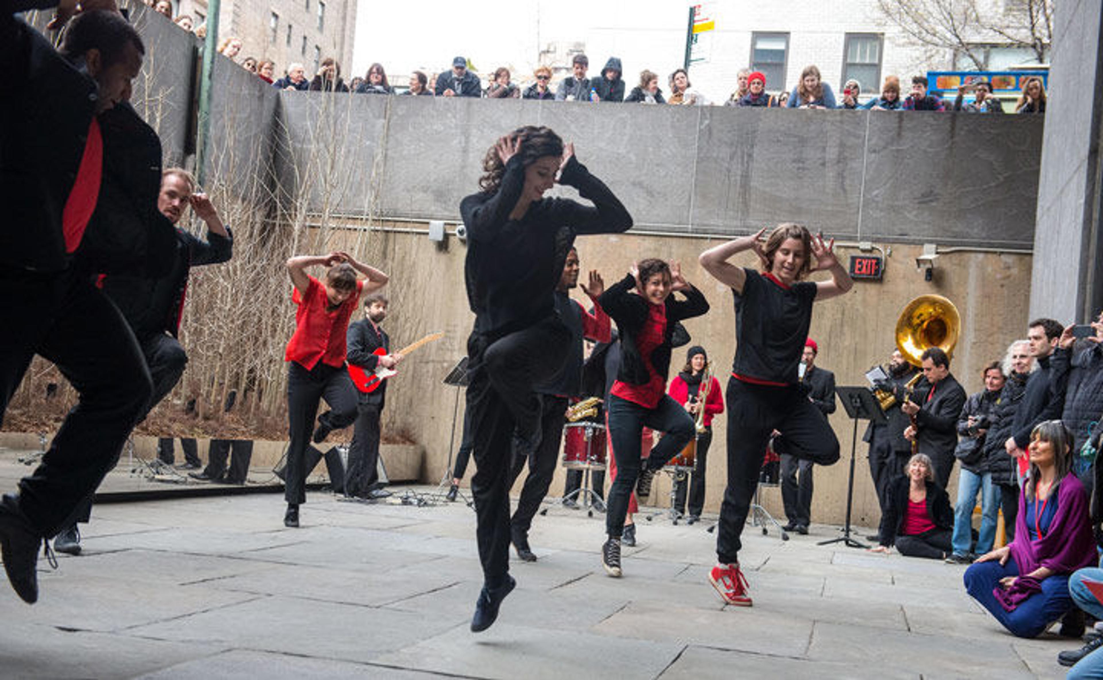 A group of dancers perform in The Met Breuer's Sunken Garden while accompanied by a brass band.