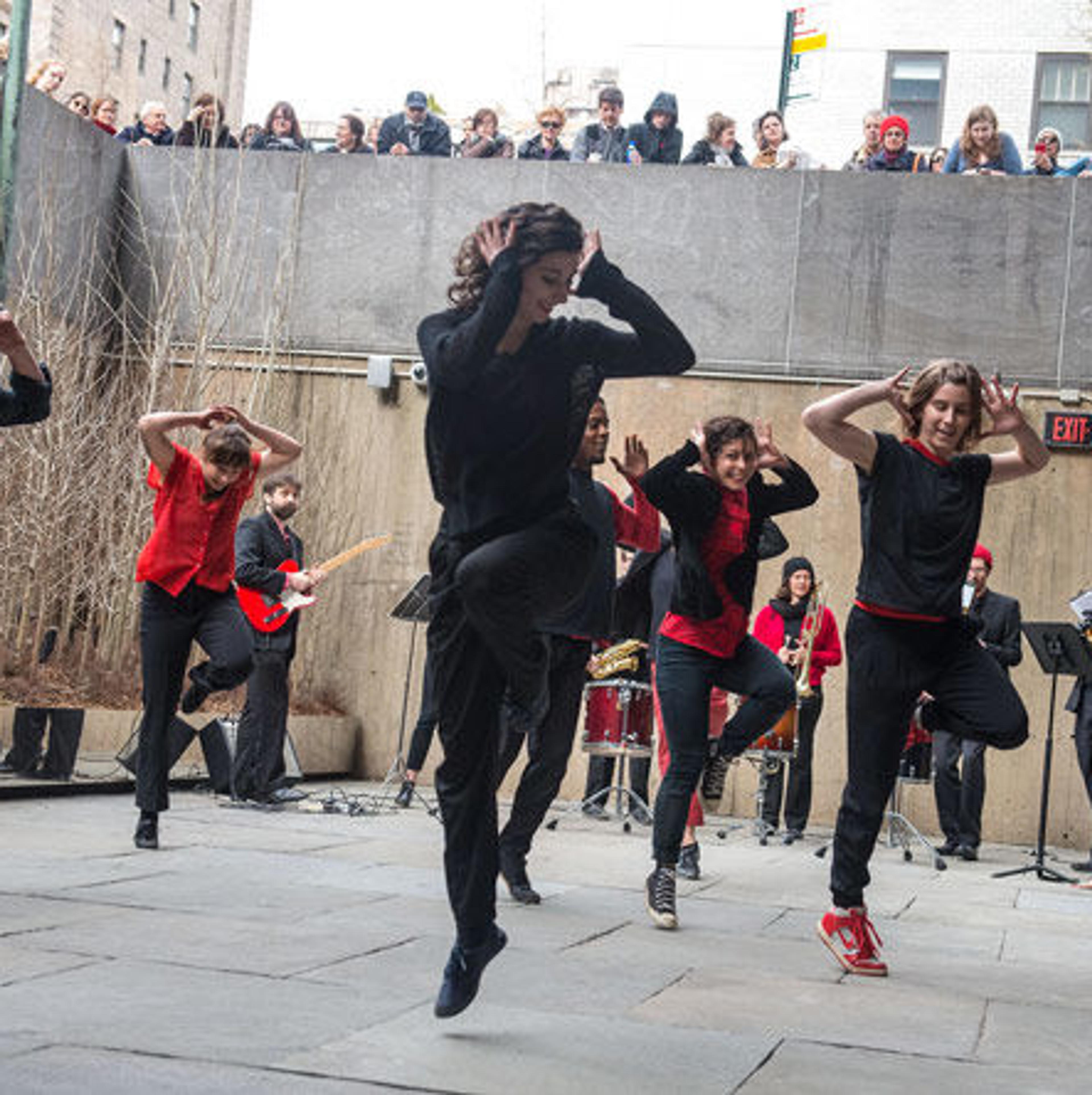 A group of dancers perform in The Met Breuer's Sunken Garden while accompanied by a brass band.
