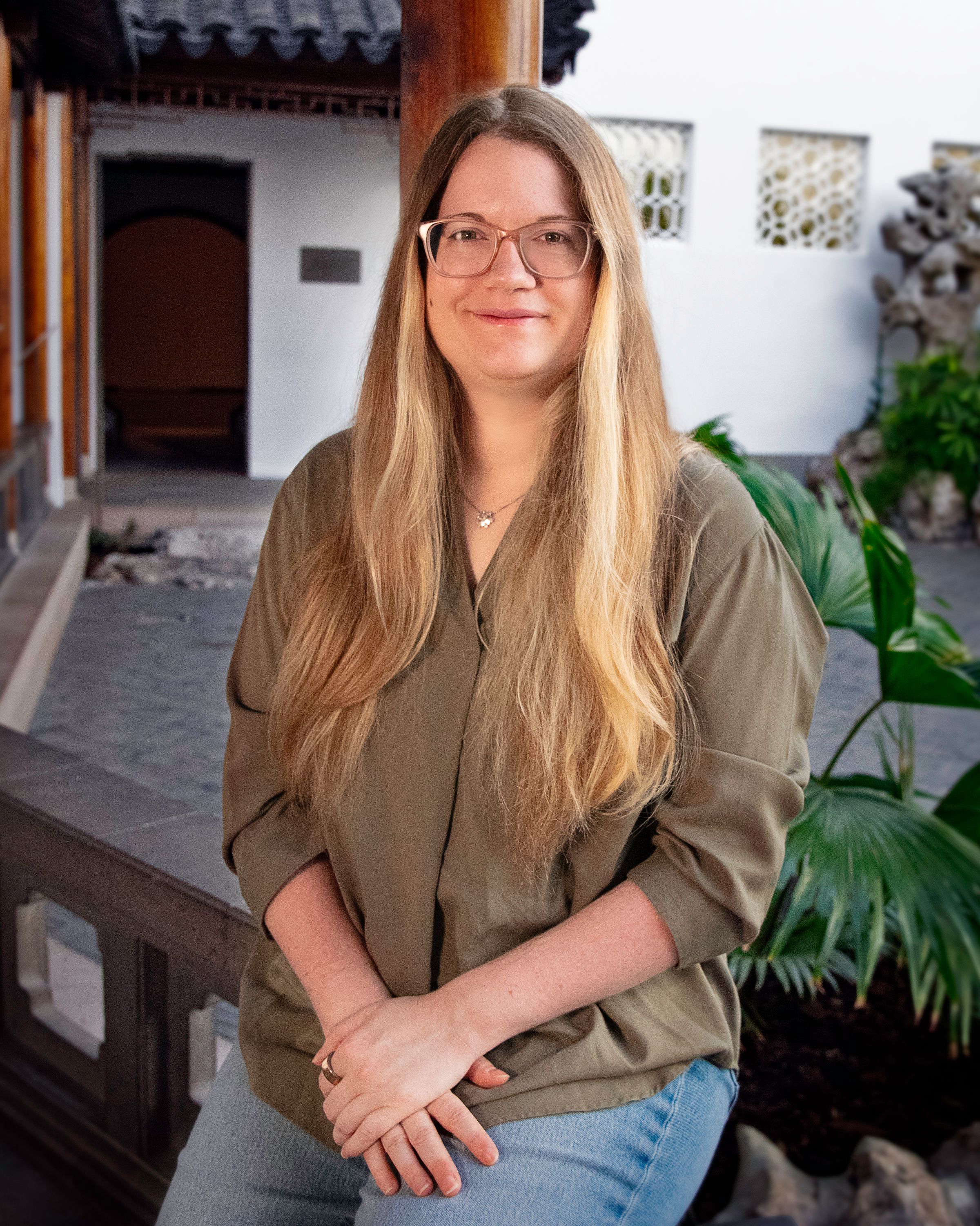Woman in an olive green shirt with glasses and long hair sit in an Asian courtyard.