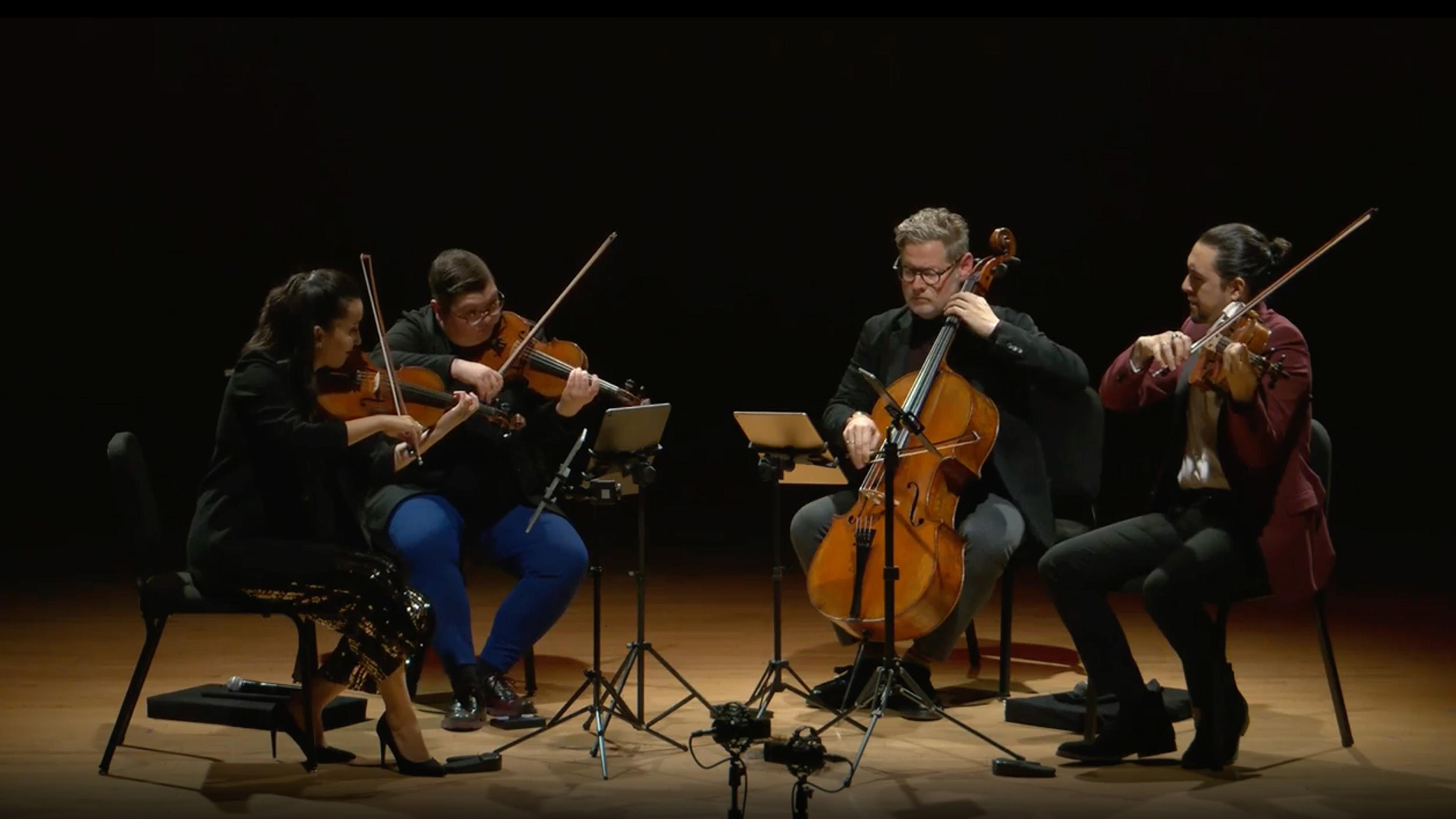 A quartet of musicians in performance on a dark stage