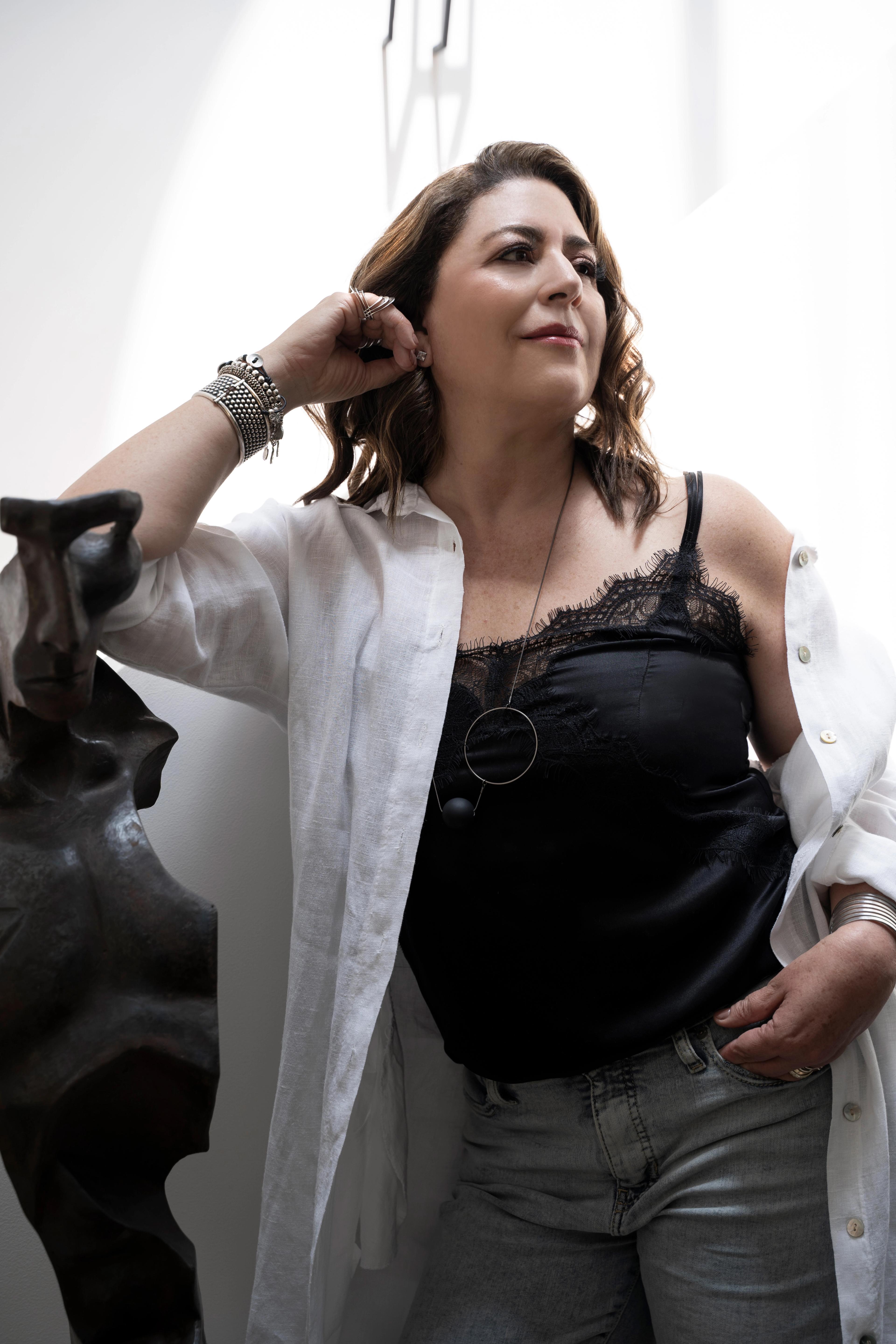 Gabriela Ortiz dressed casually, leaning against a black sculpture and gazing into the distance.