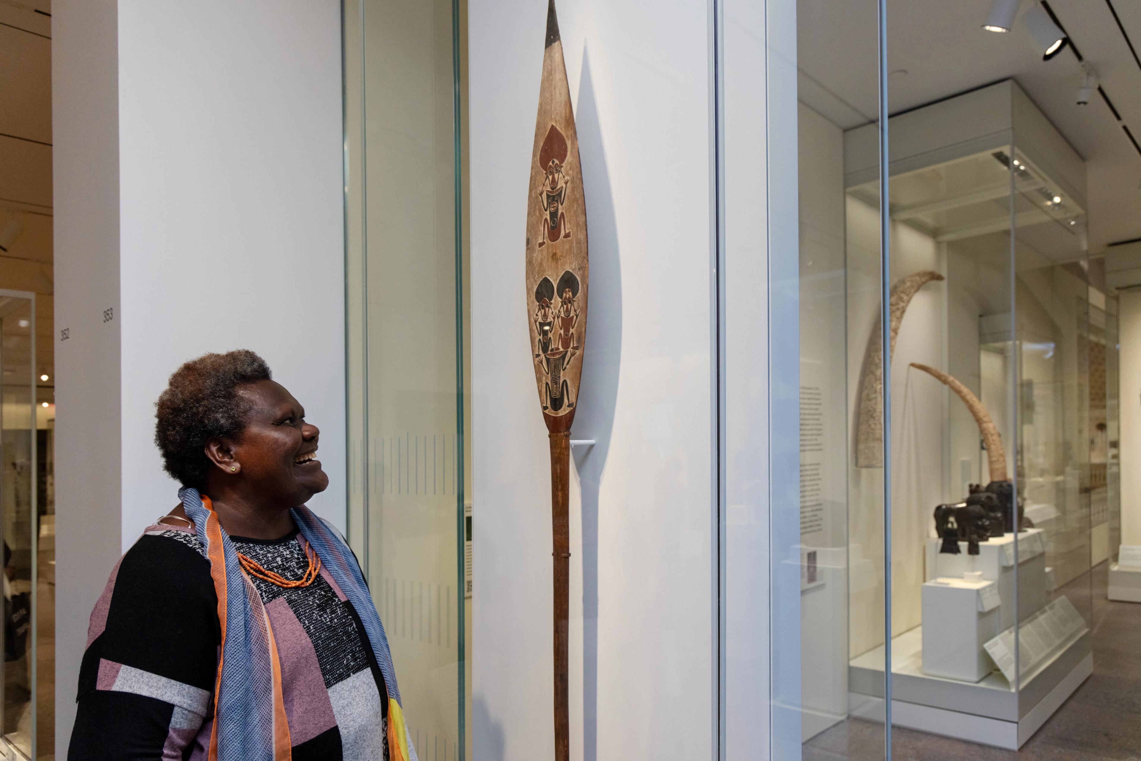 Sana Balai standing in front of a ceremonial paddle in the Oceania galleries at The Met.