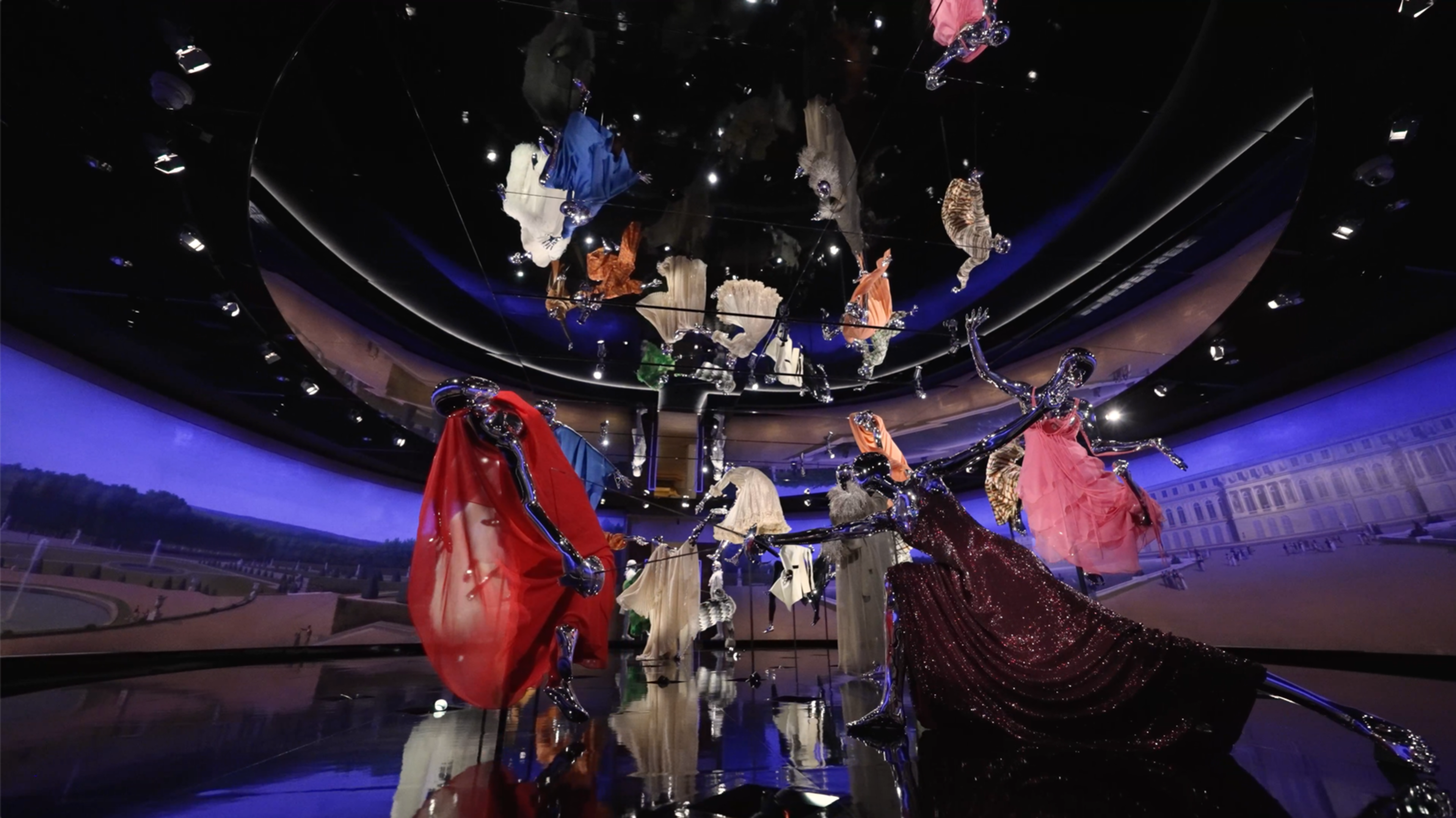 Installation shot of this year's Costume Institute exhibition, featuring a group of chrome mannequins in haute couture caught in a battle, surrounded by a panoramic painting of Versailles