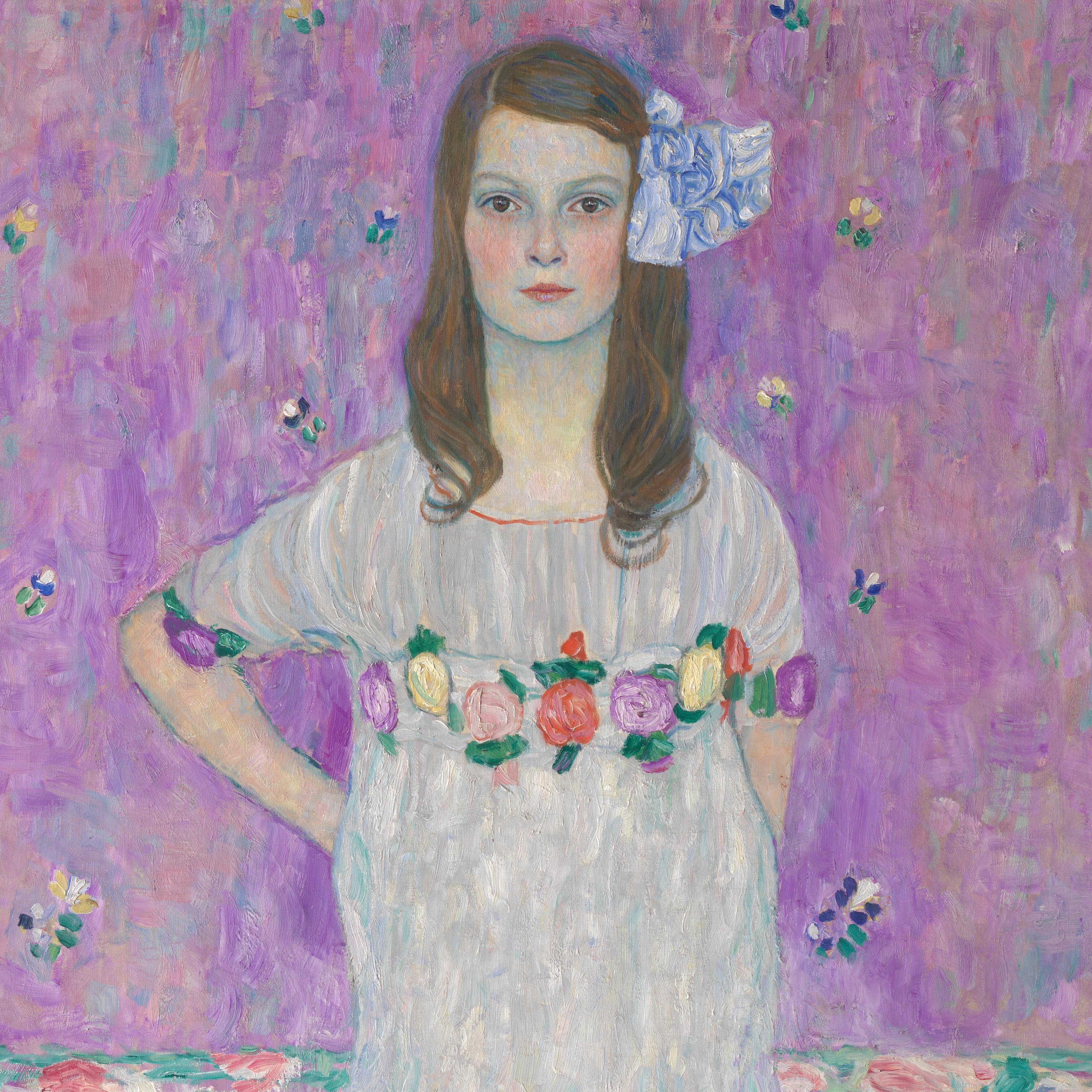 A young girl poses with a stoic face and a hand on her hip. Her dress and hair are accented with flowers.