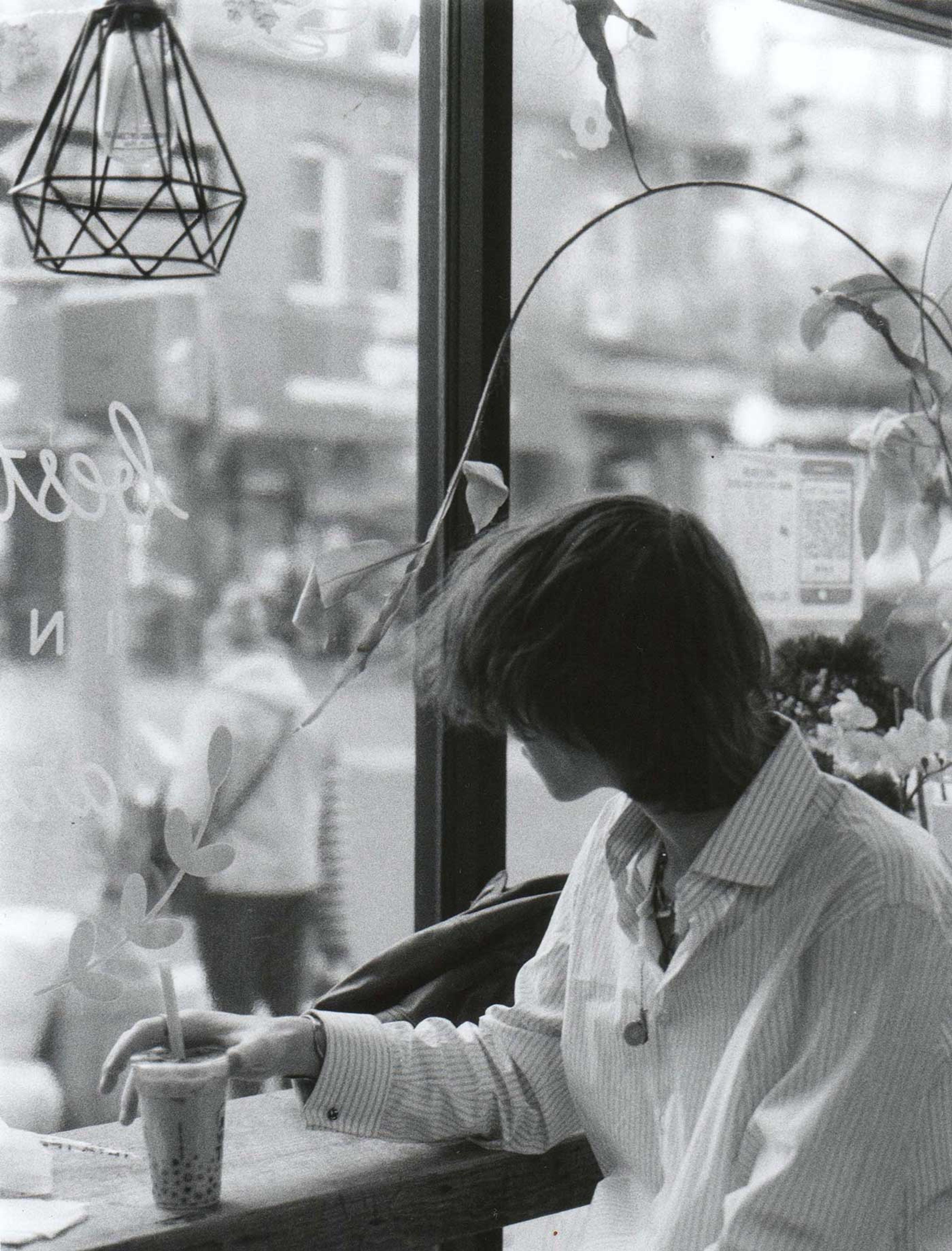 Photograph of a person drinking tea while looking out a shop window.