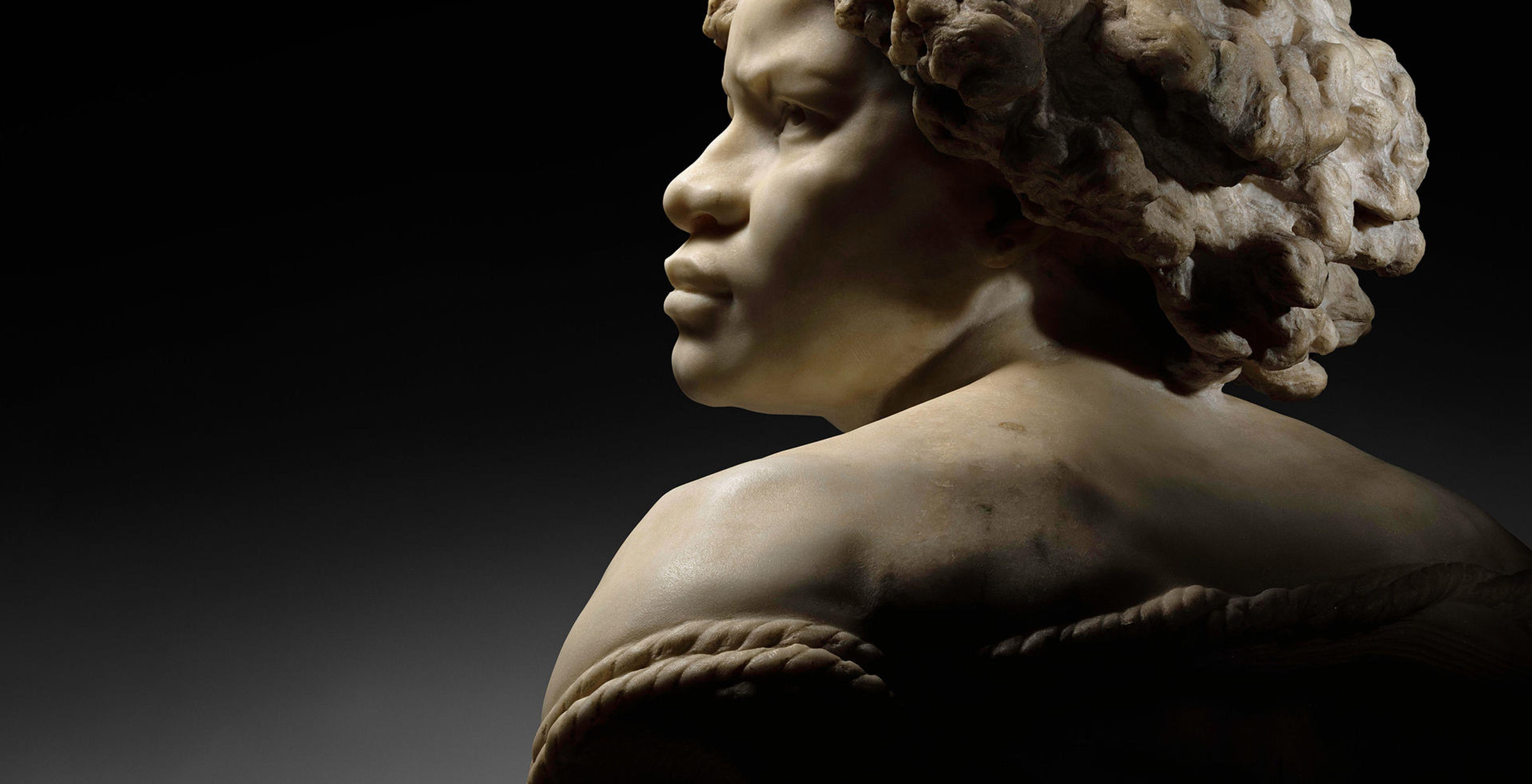 A high-contrast view of Jean-Baptiste Carpeaux's "Why Born Enslaved!" from behind with her profile showing