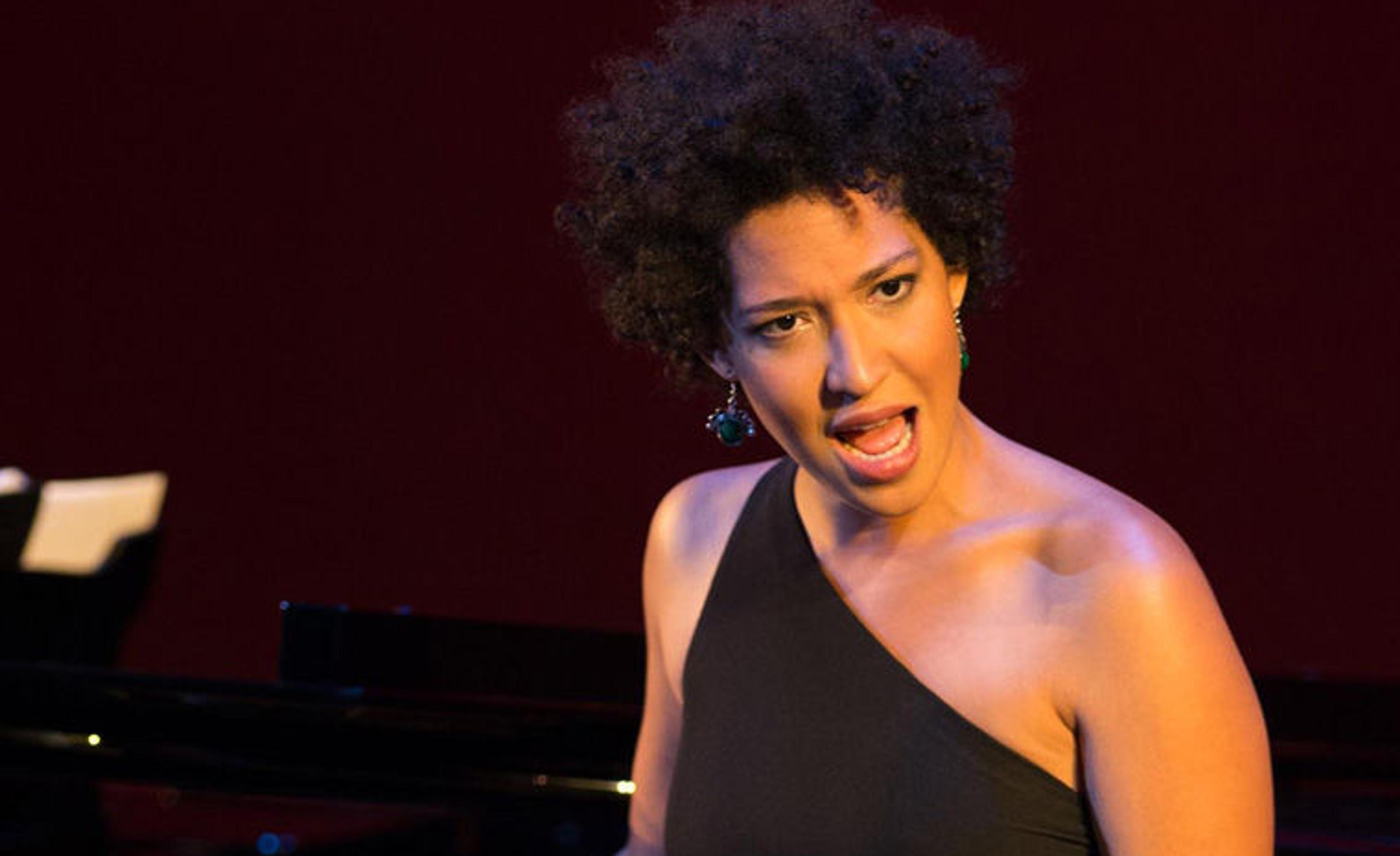Julia Bullock wearing a black dress and singing in front of a grand piano
