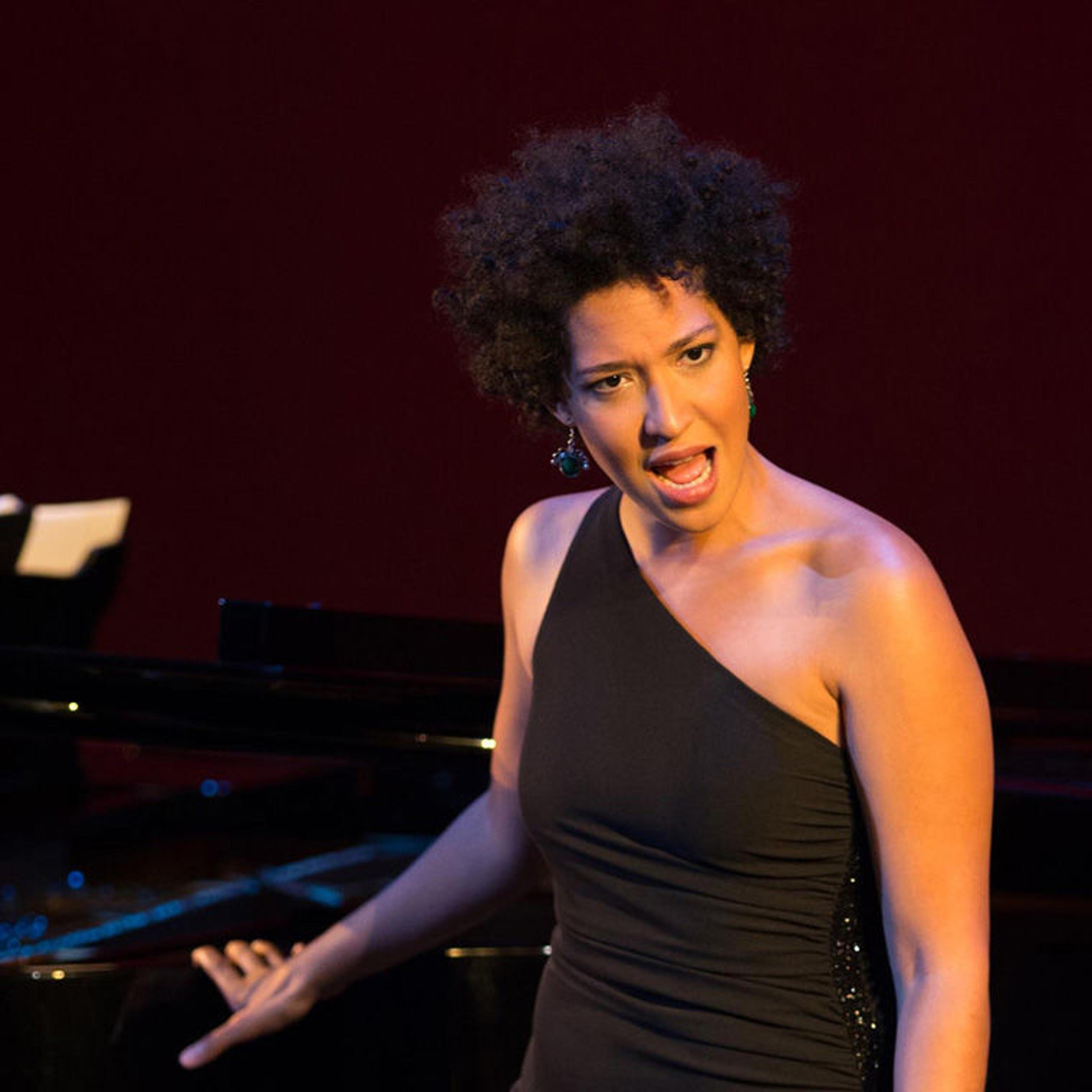 Julia Bullock wearing a black dress and singing in front of a grand piano