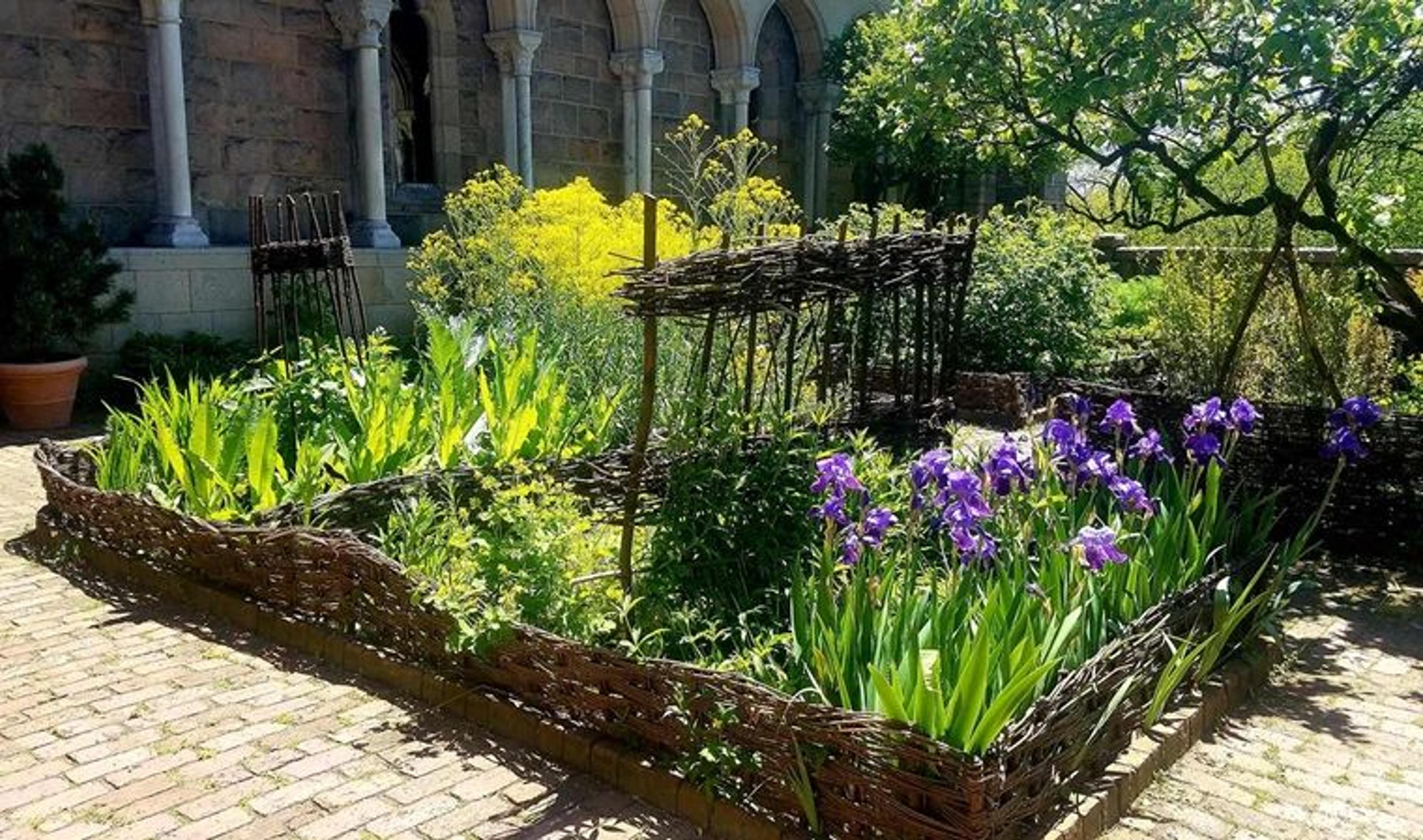 A garden bed full of flowers and herbs situated in a medieval cloister.
