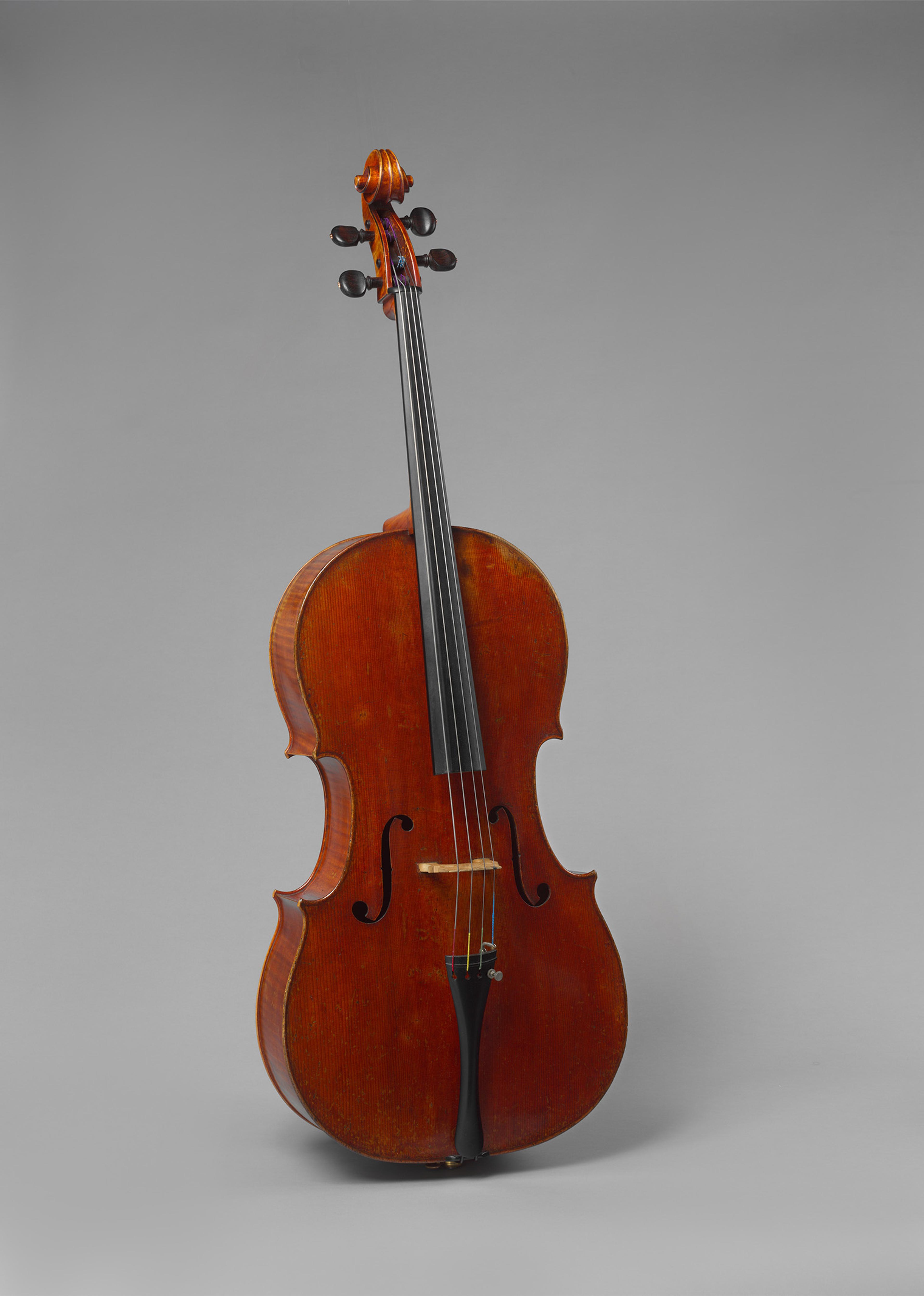 A classic, polished cello stands upright against a plain gray background, showcasing warm, rich wood tones and elegant curves, evoking sophistication.
