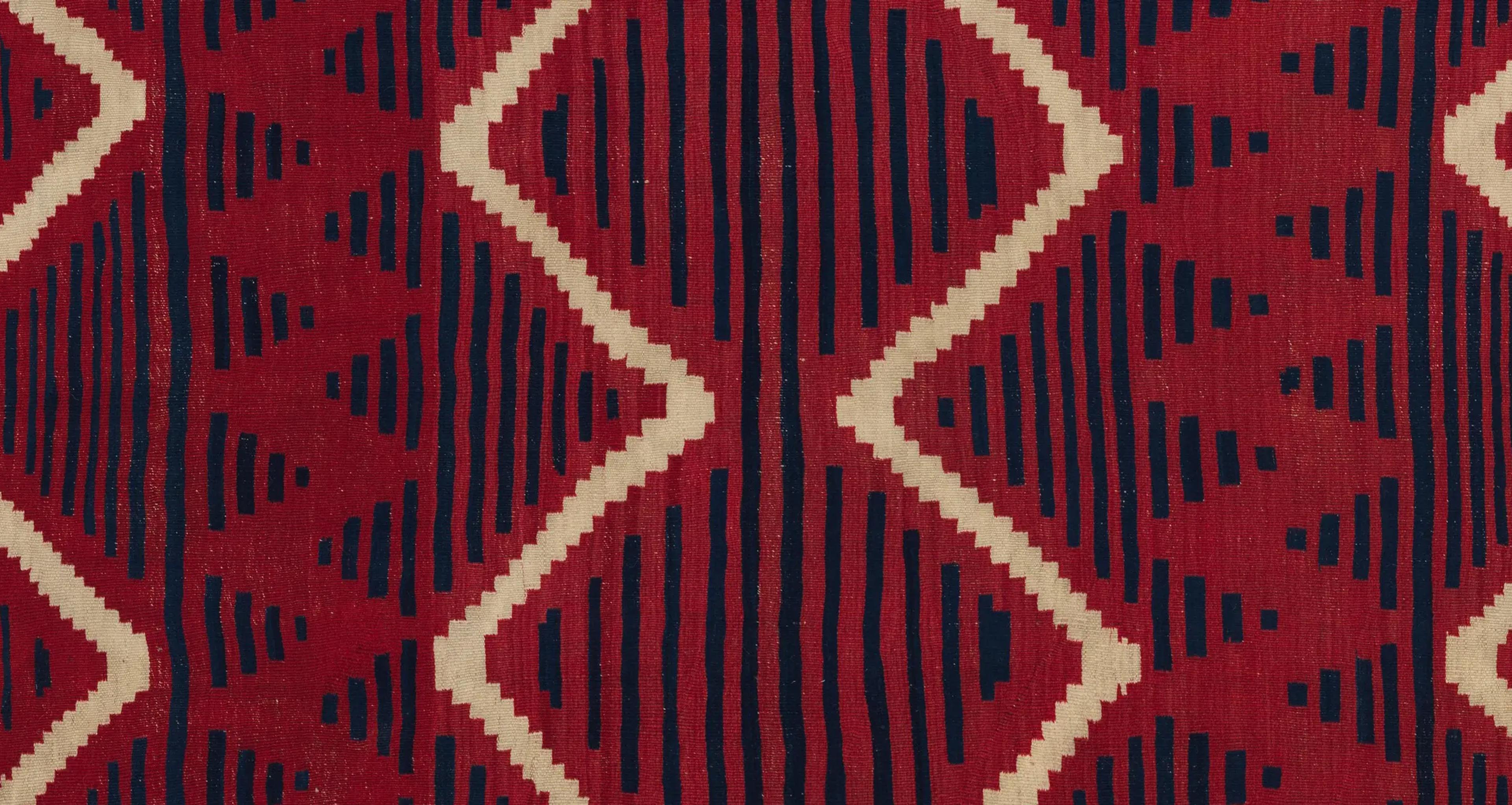 A detail of a red woven serape with abstracted black and cream lines running throughout.
