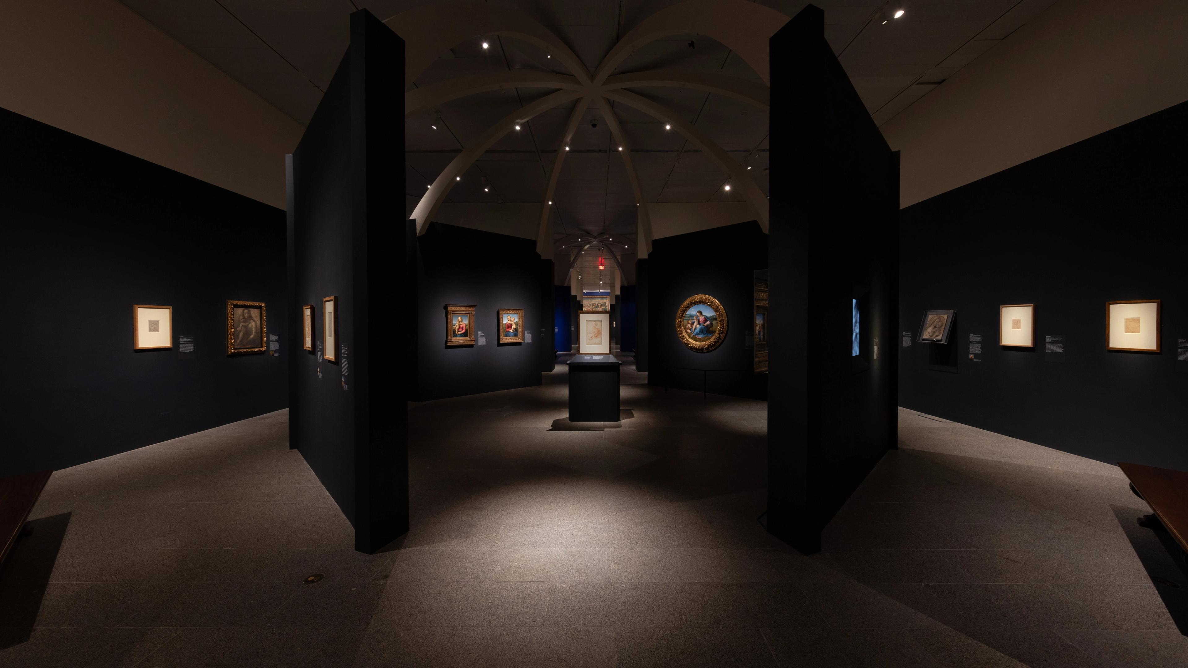 A dimly lit art gallery showcases framed artwork on dark walls