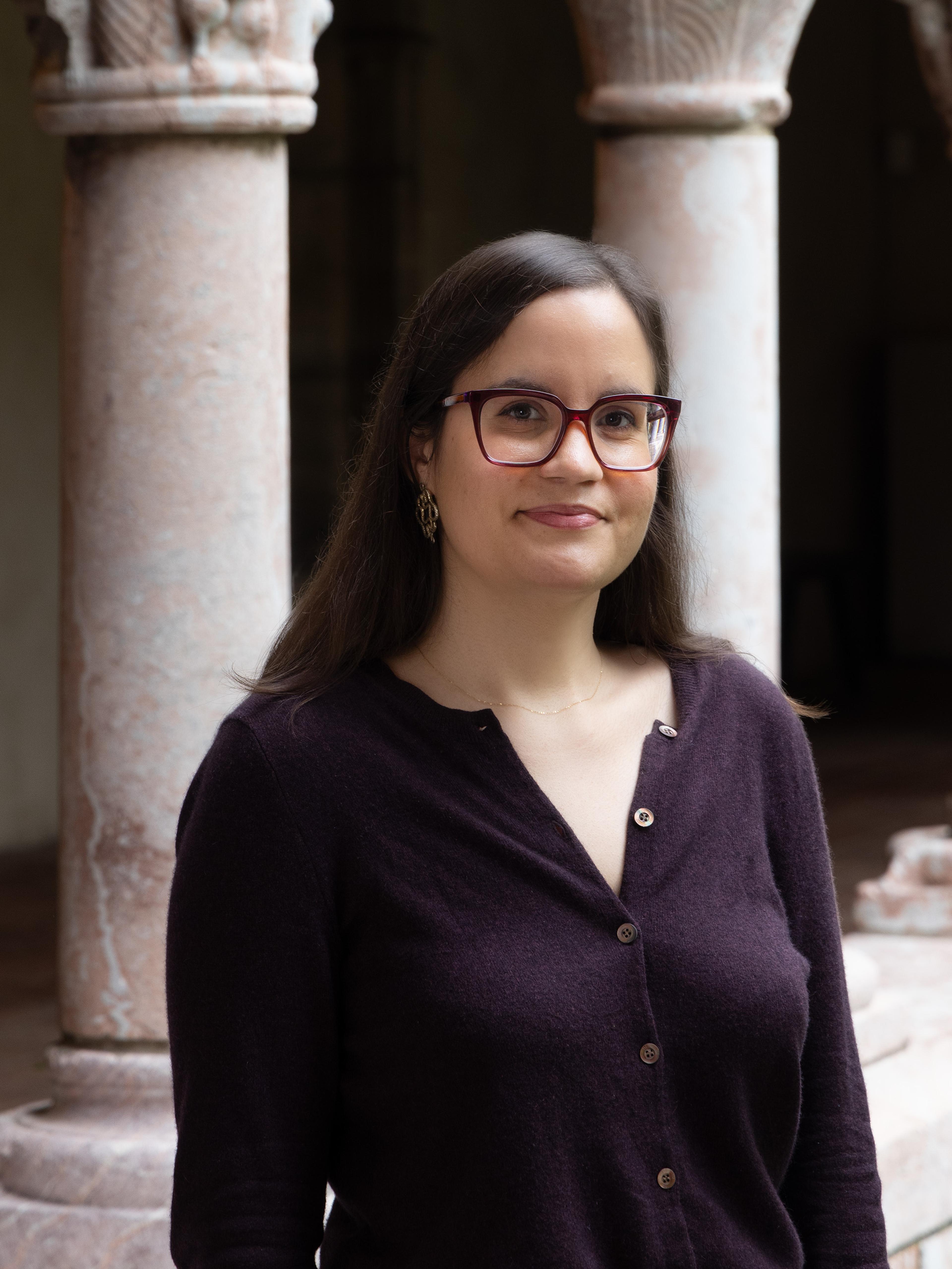 A woman wearing a dark blouse and glasses poses in front of a marble archway