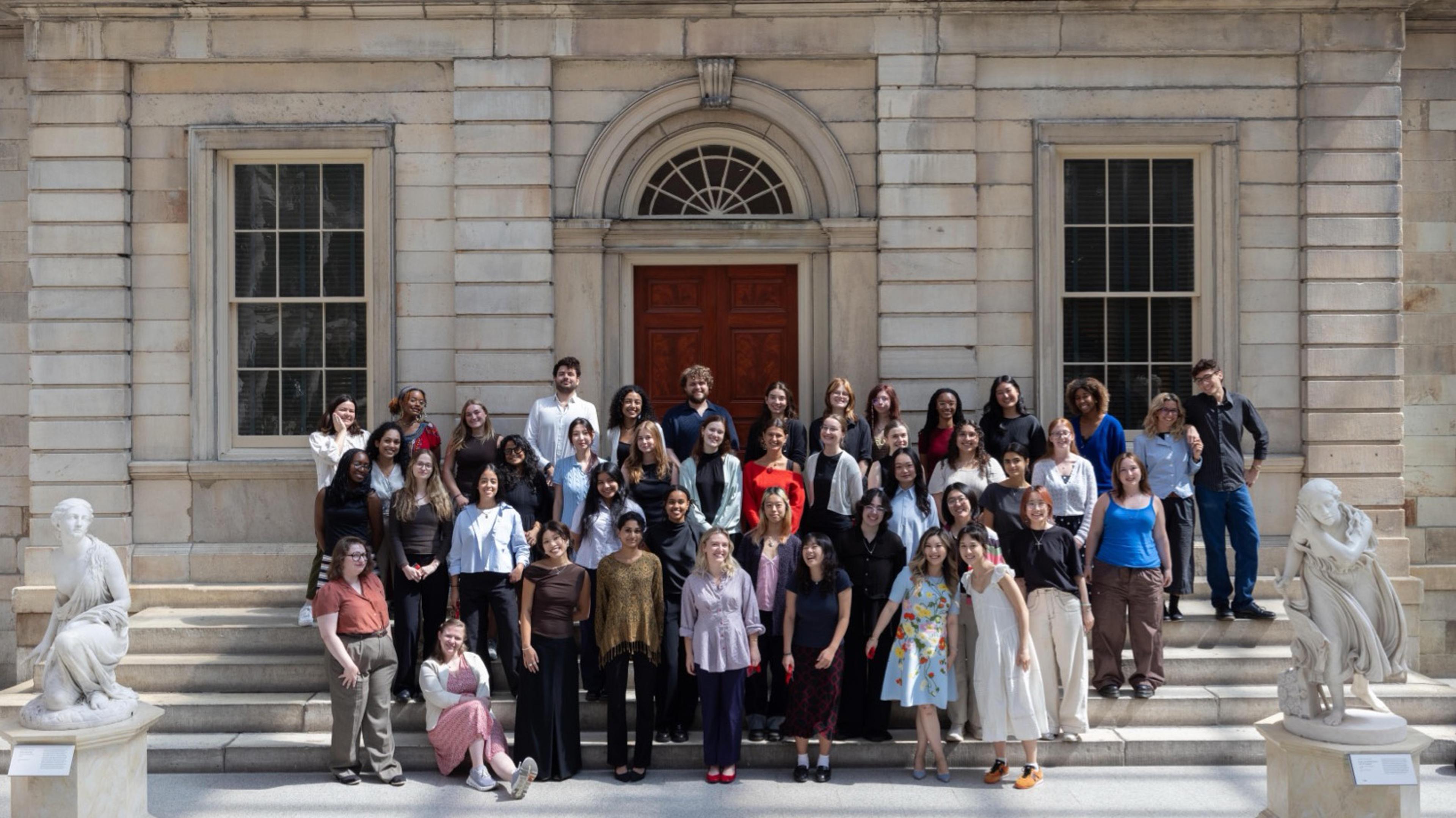 A group of interns posing in front of a stone facade in The Met's American Wing.