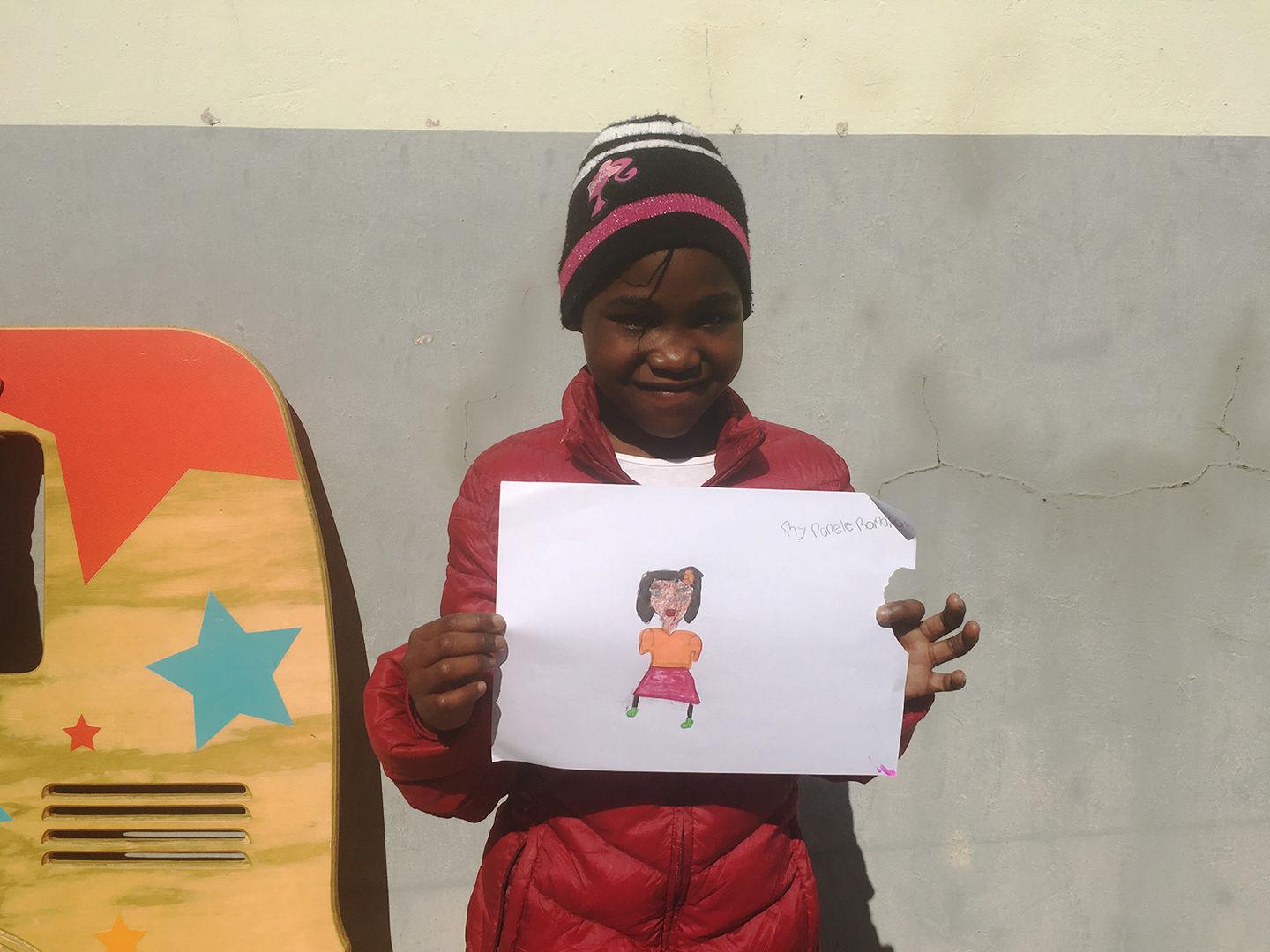 Ponele smiles as she holds up the finished portrait of her mom outside in the sunlight.