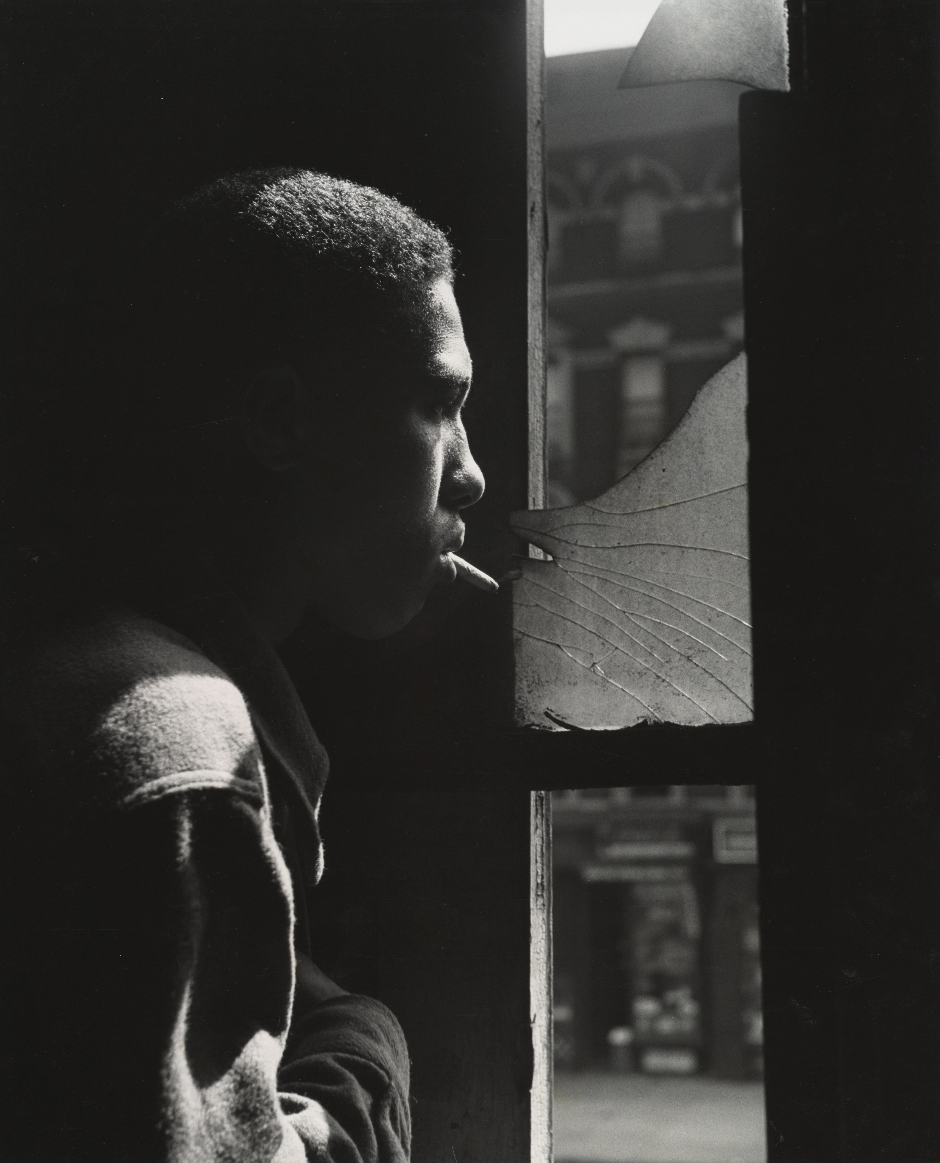 Black and white photograph of a man smoking and standing at a window.