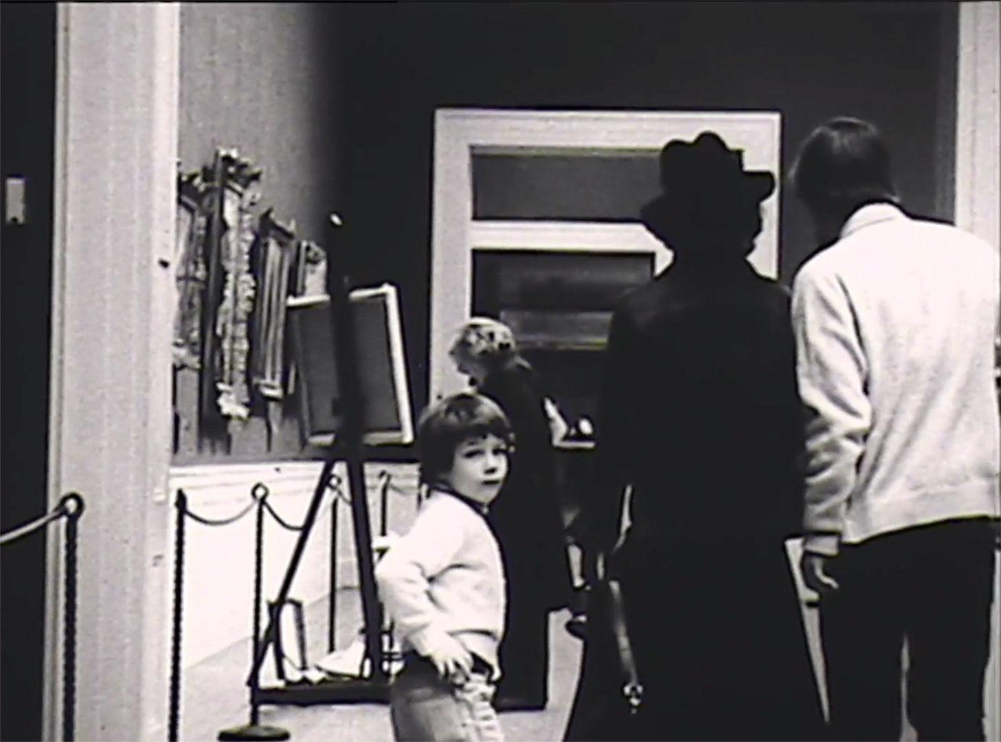 A black and white photo of a family at the museum, and the child looks at the camera