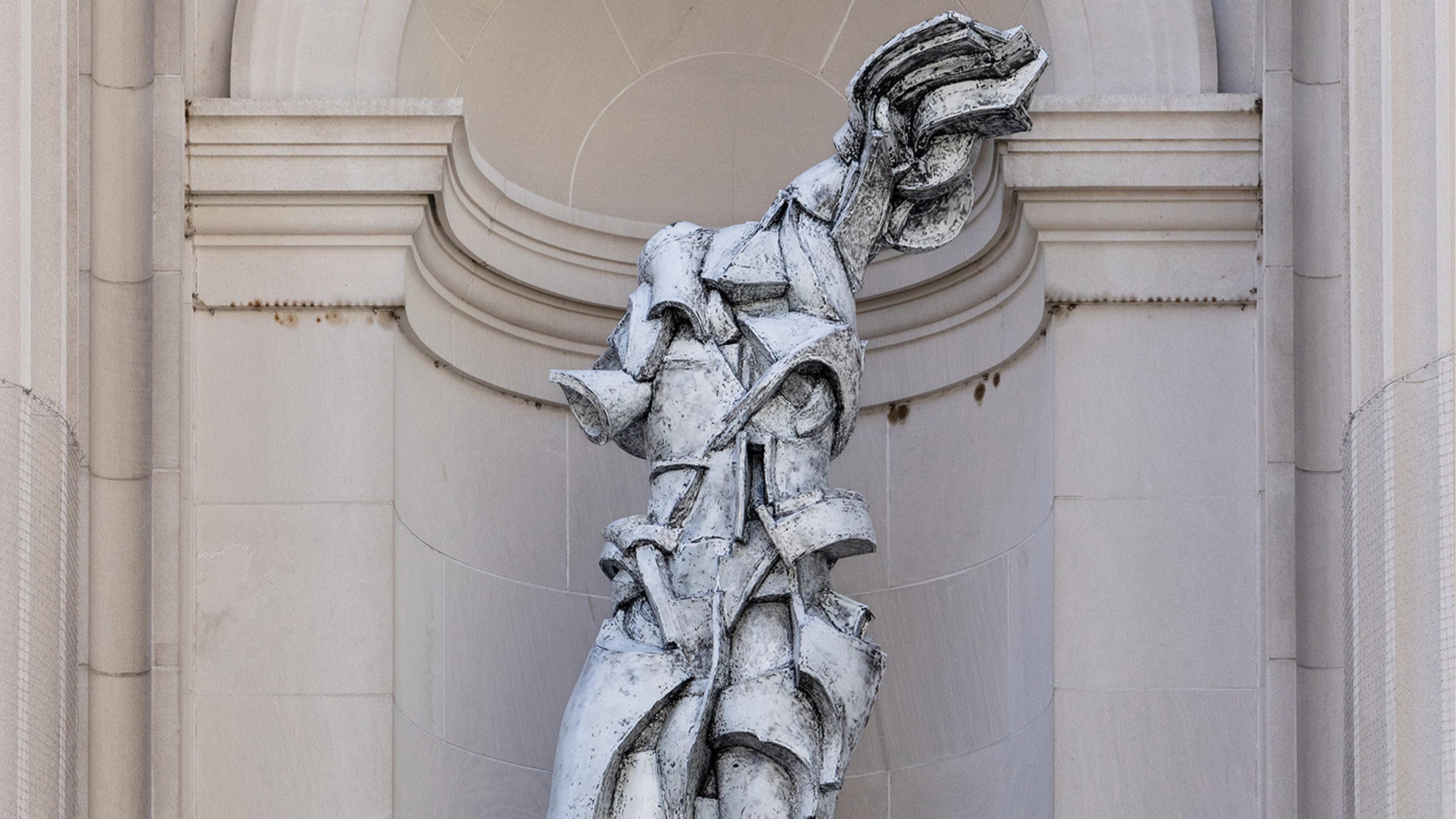 Futuristic sculpture of a fragmented, abstract human form in stone against a neoclassical arch. The tone is dynamic and modern amidst classical architecture.