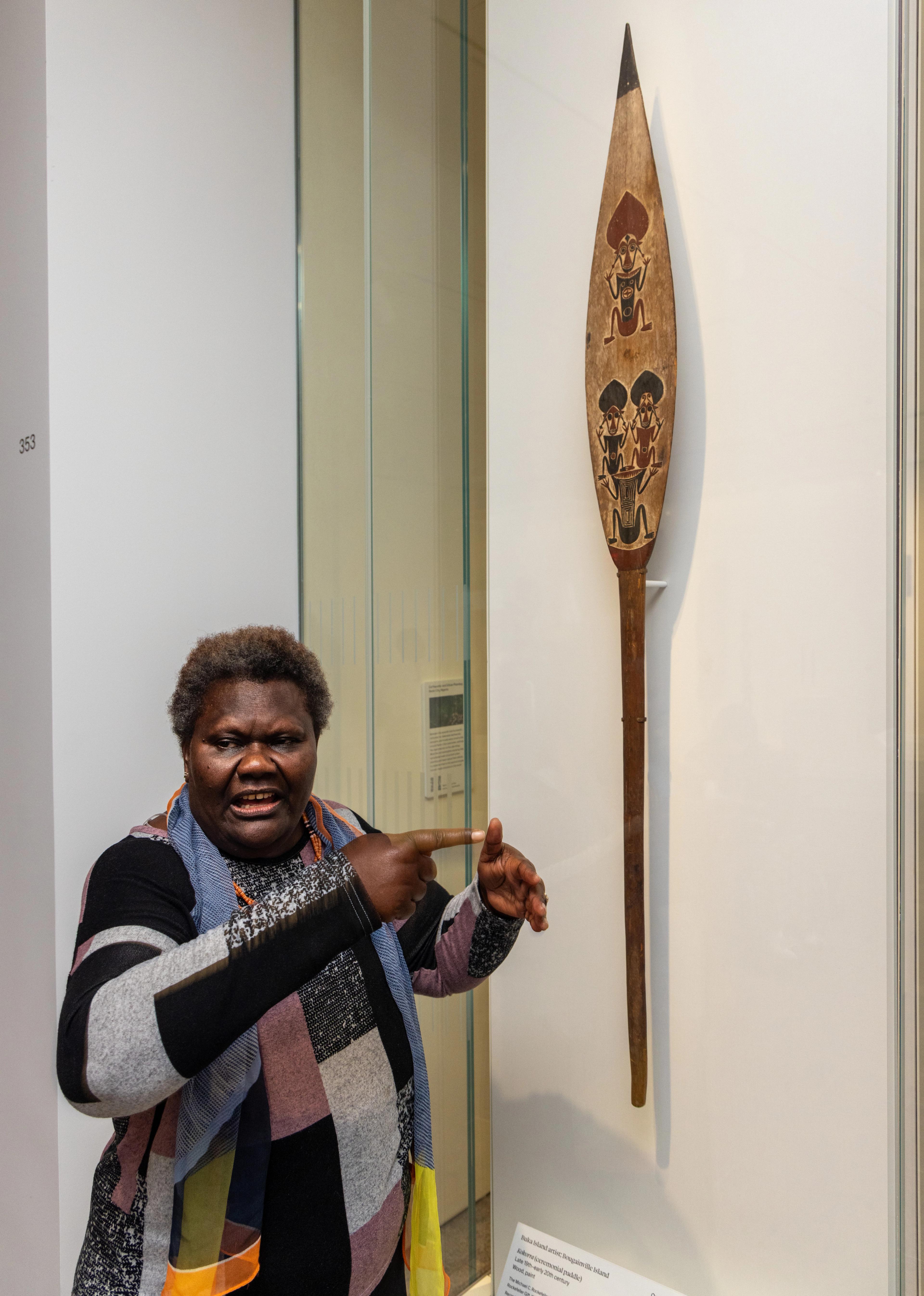 Sana Balai standing in front of a ceremonial paddle in the Oceania galleries at The Met.