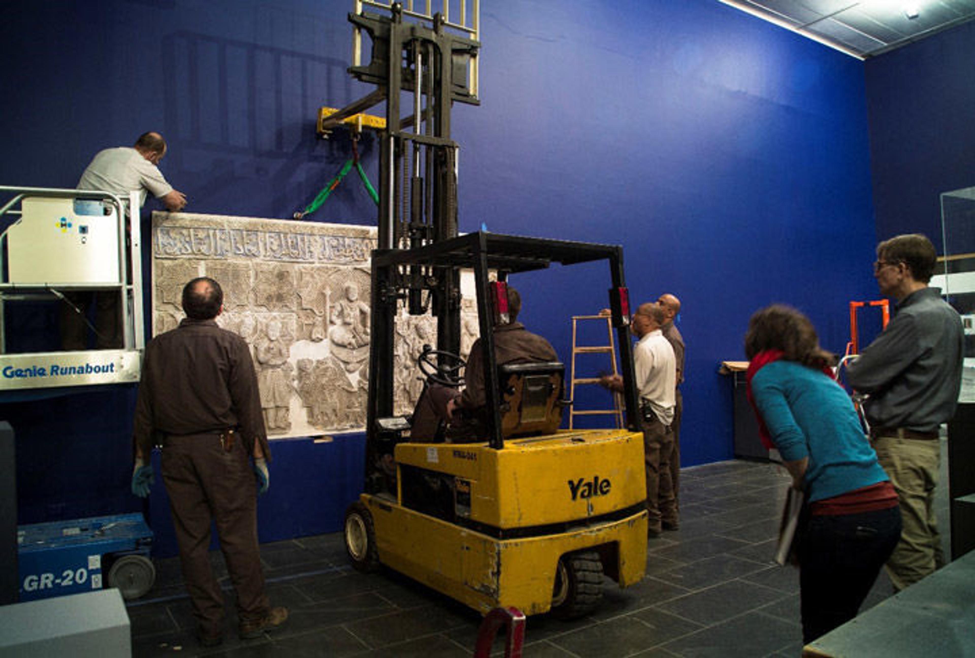 A group of Museum staff work together to install a large stucco panel in an exhibition gallery
