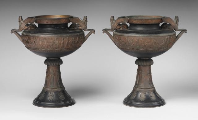 Photograph of two bronze urns with detailed Assyrian scenes on the bowl and stem