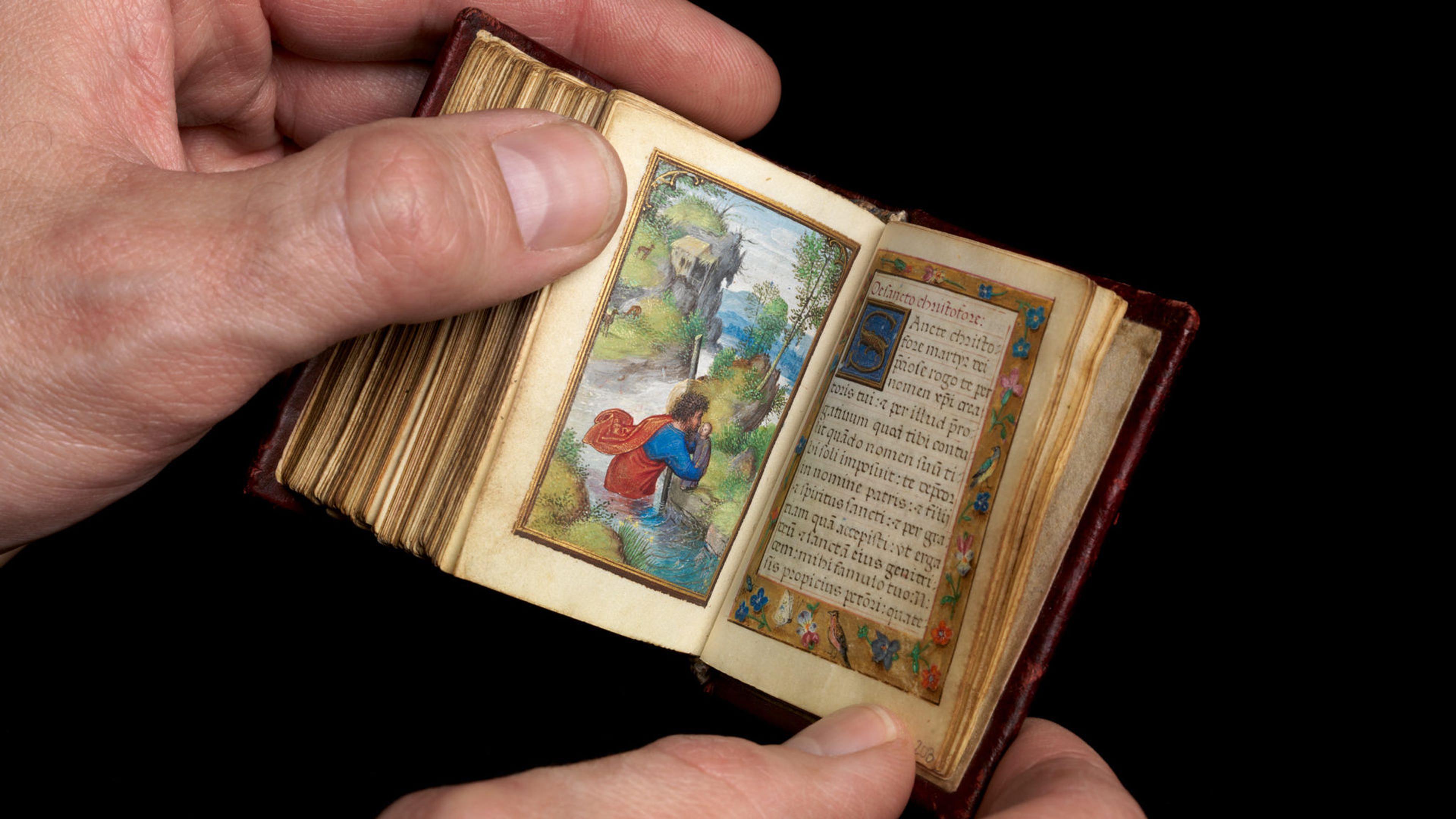 Hands holding a miniature book with colorful illustrations and calligraphy